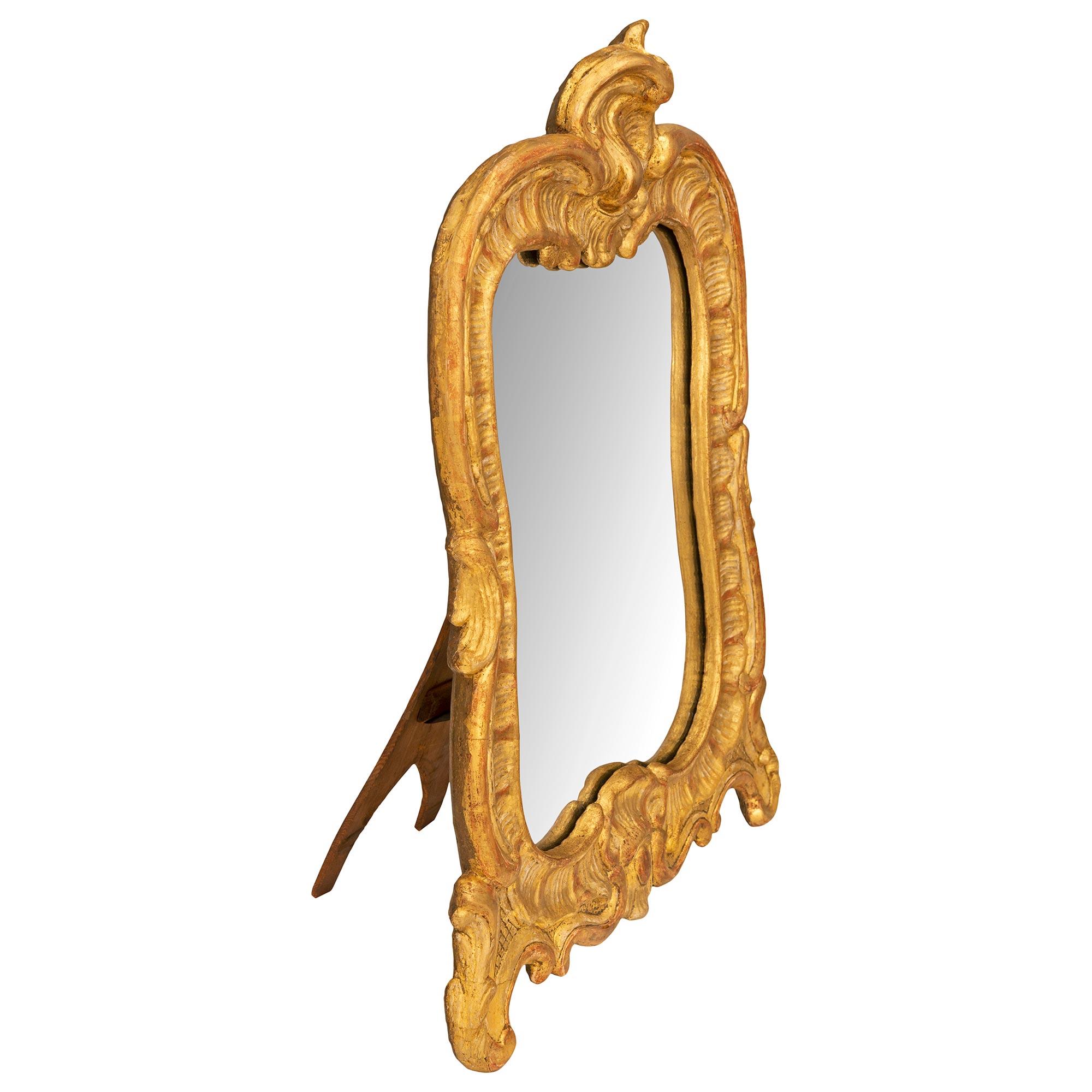 Magnifique miroir de courtoisie en bois doré d'époque Louis XV du XVIIIe siècle. La plaque de miroir est encadrée dans un joli cadre en bois doré festonné, avec de fins pieds à volutes décorés d'étonnants motifs de treillis centrant une réserve de