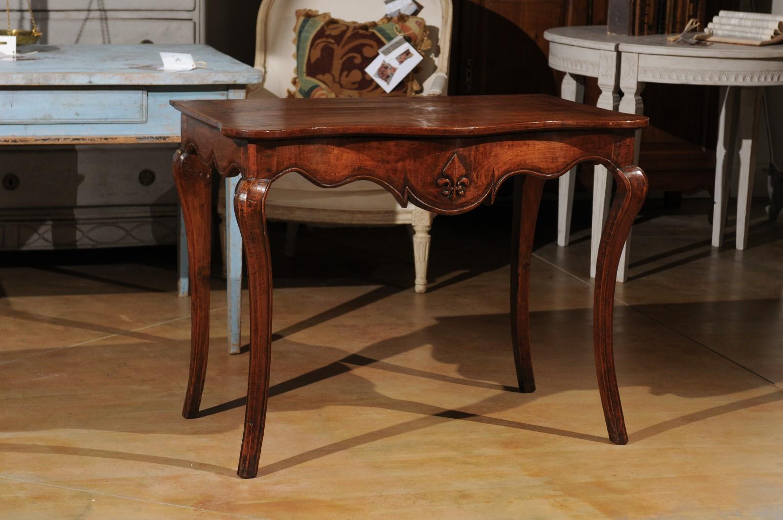 A French Louis XV period Provençale console table from the 18th century, with scalloped apron, stylized fleur-de-lys and cabriole legs. Born in Provence during the reign of King Louis XV le Bienaimé (the Beloved), this exquisite console table