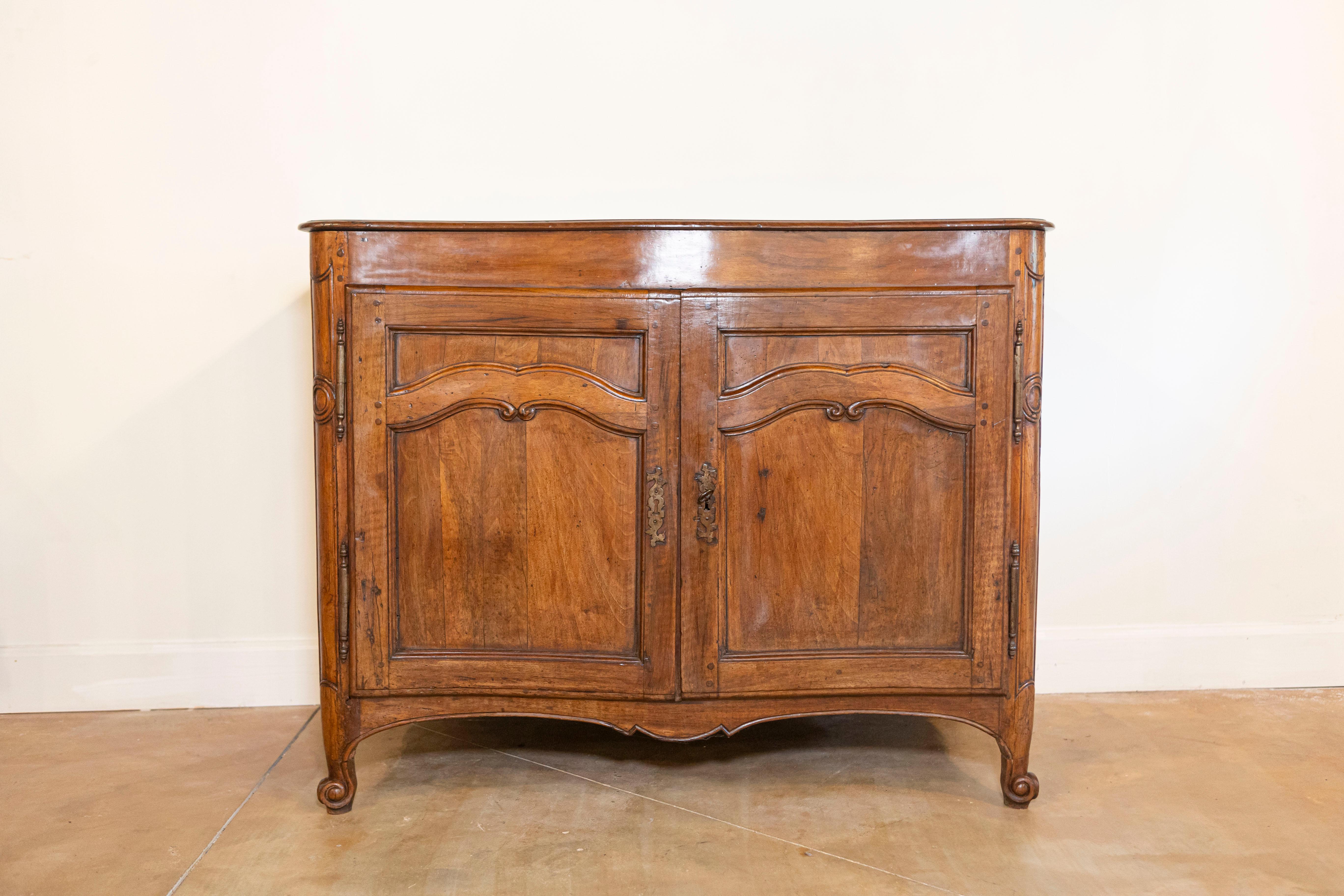 A French Louis XV period walnut buffet from the 18th century with two doors and carved arching accents. Immerse yourself in the timeless allure of French Louis XV design with this walnut buffet from the 18th century. Crafted with exquisite attention