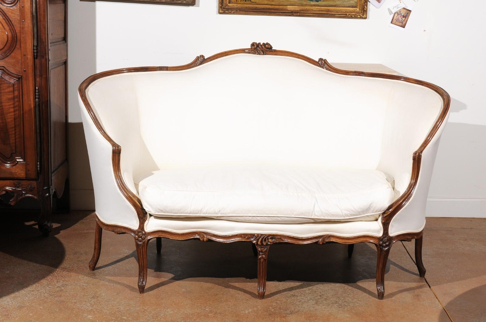 A French 18th century Louis XV period walnut wraparound sofa from Lyon, with upholstery and cabriole legs. Born in the Rhône Valley during the 18th century, this exquisite canapé features a wraparound back, accented on its upper rail with two