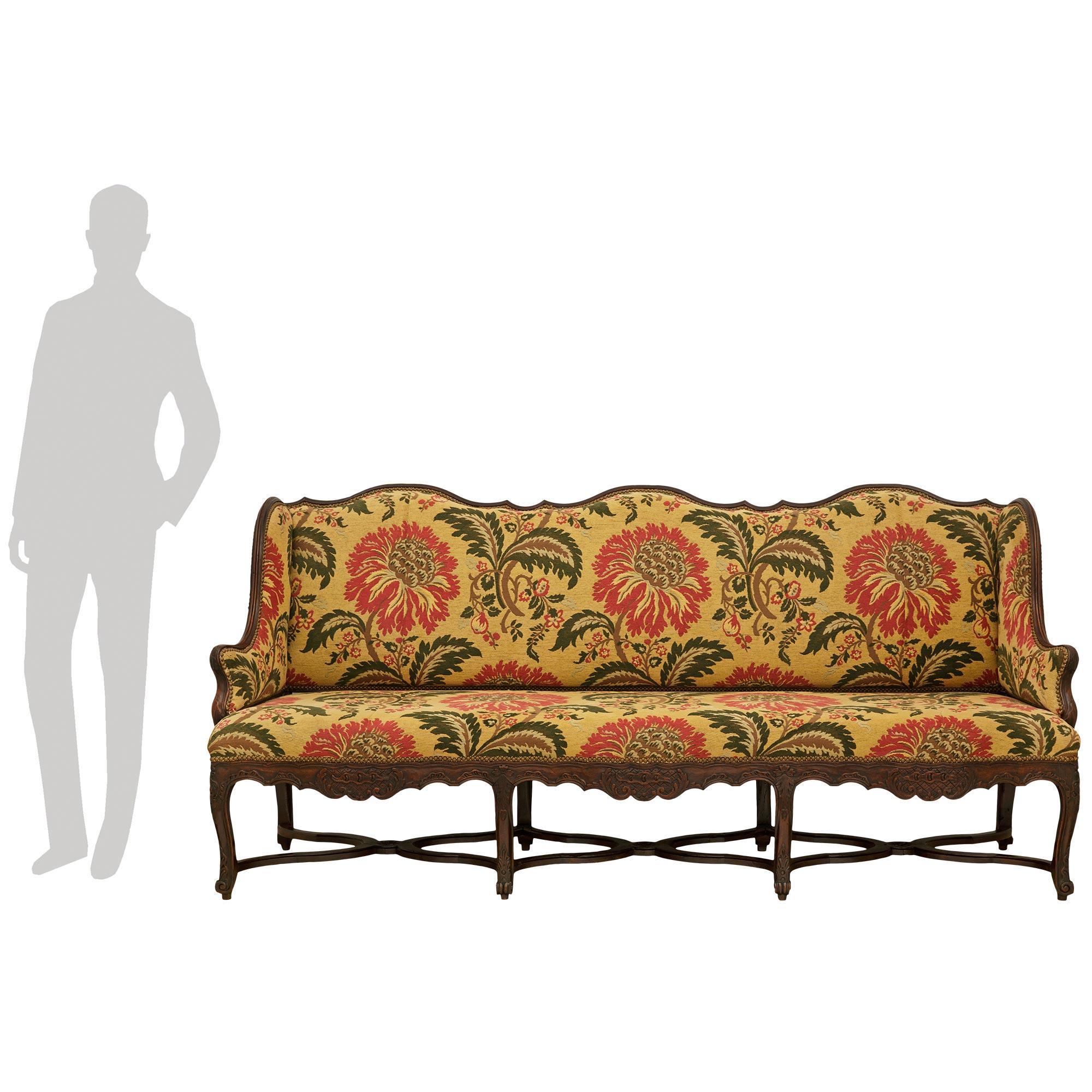 An impressive and most decorative French 18th century Louis XV Period Walnut settee. This stunning winged settee is raised on eight richly carved cabriole legs with bottom acanthus leaves and top cabochons amidst scrolled designs, while joined by