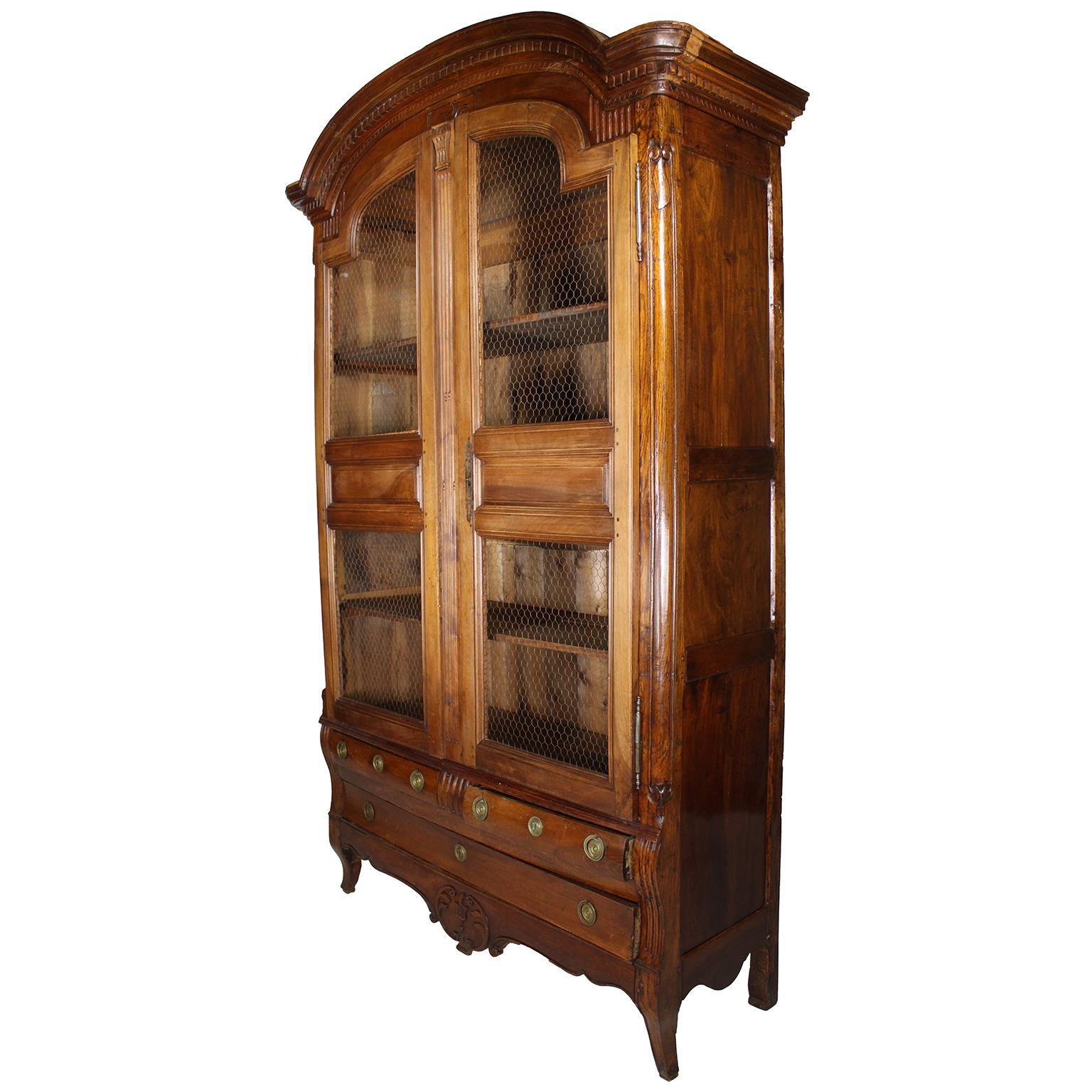 A Tall French 18th-19th Century Louis XV Style Provincial - Country French Carved Walnut Armoire - Bibliotheque - Bookcase. The twin-door vitrine or book cabinet with three wooden shelves and chicken-wire protective doors, above a pair of side by