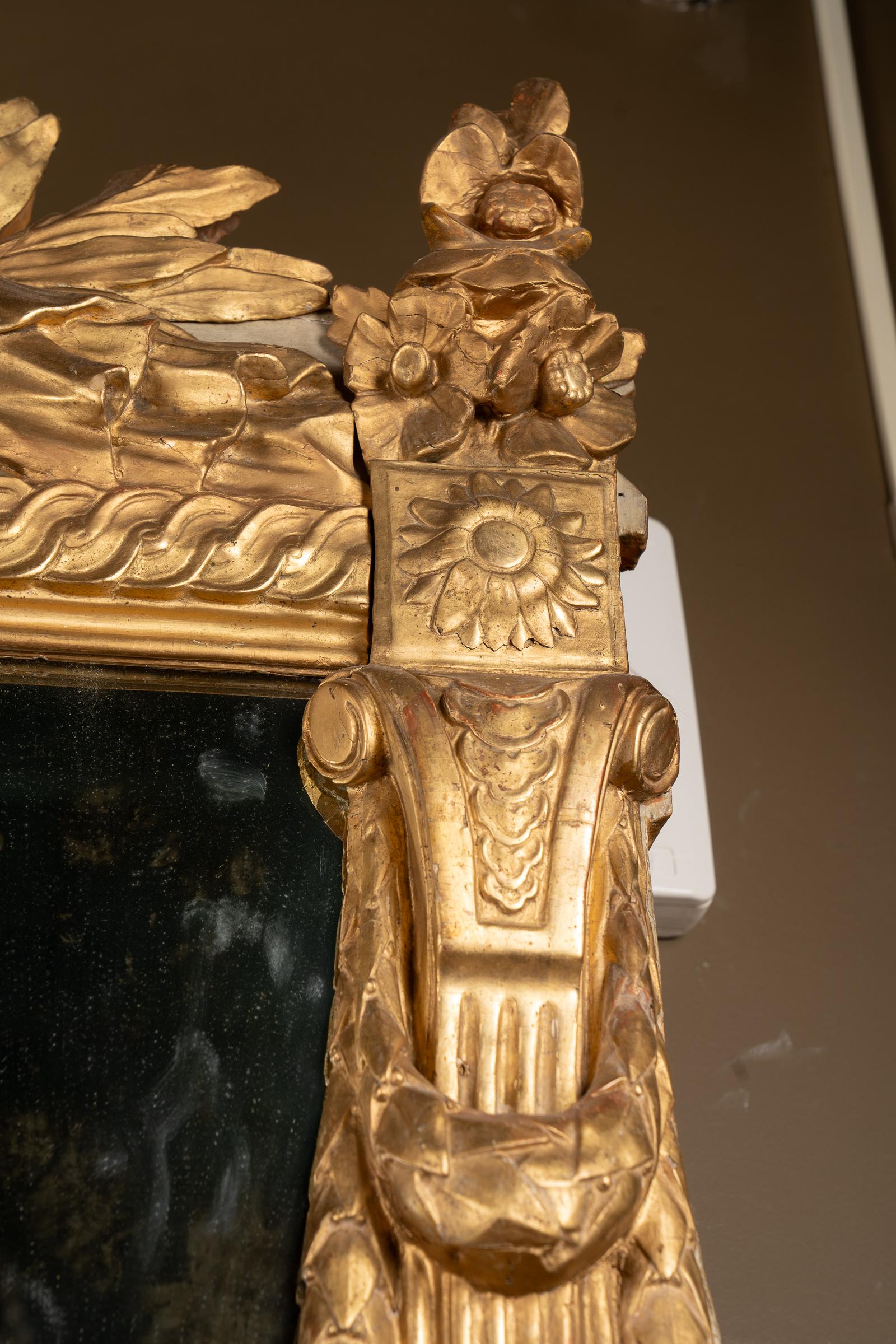 Ce miroir français de style Louis XVI est orné de lourdes sculptures et est peint à la feuille d'or. Le miroir en bois doré du XVIIIe siècle présente un magnifique motif.  Il est orné d'une urne centrale, de fleurs et de guirlandes magnifiquement