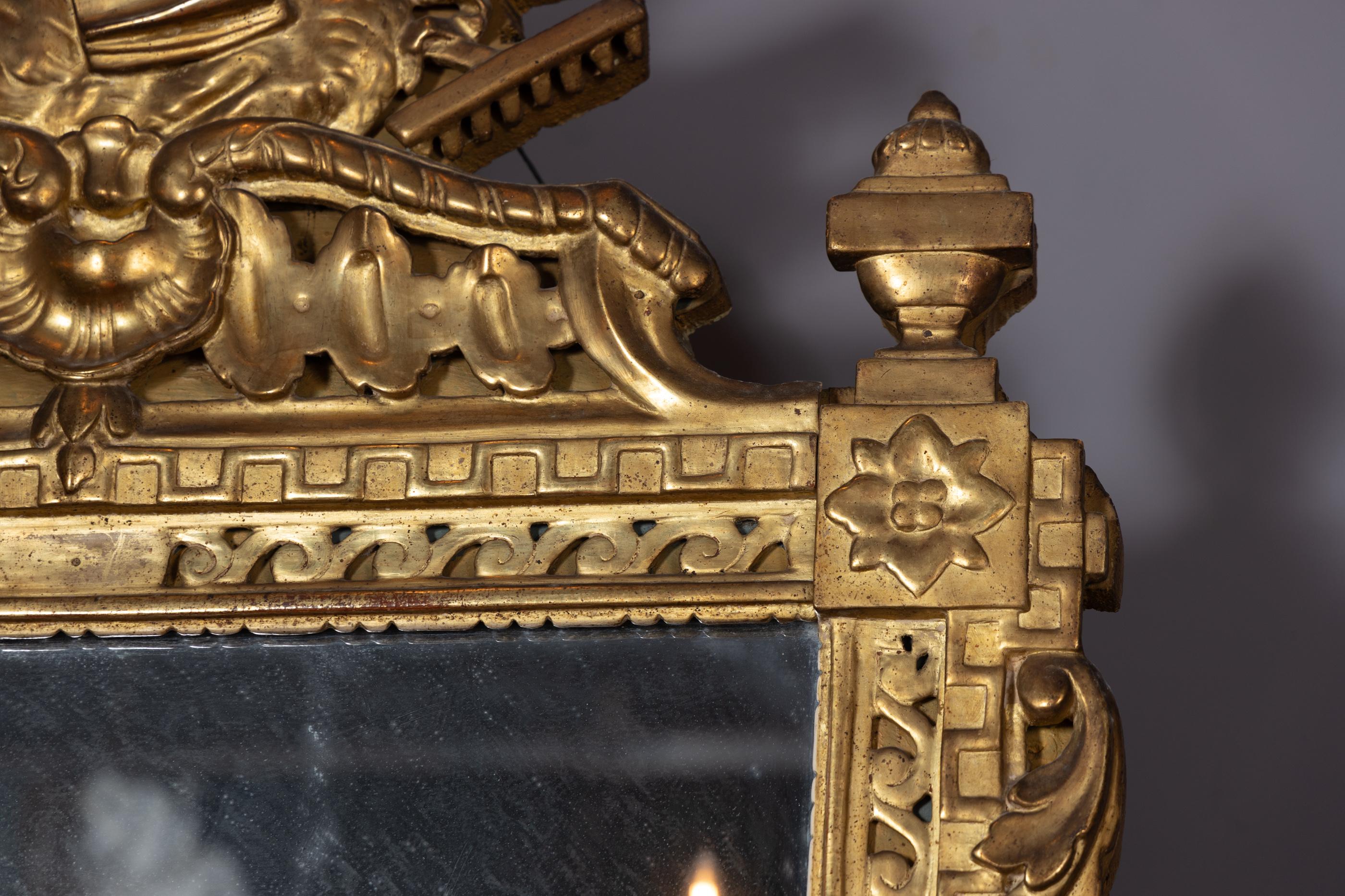 Ce miroir d'époque Louis XVI est magnifiquement sculpté à la feuille d'or et surmonté d'instruments de musique. Cette pièce antique française date du 18e siècle et présente un plateau, des côtés et un fond fortement sculptés. La pièce est