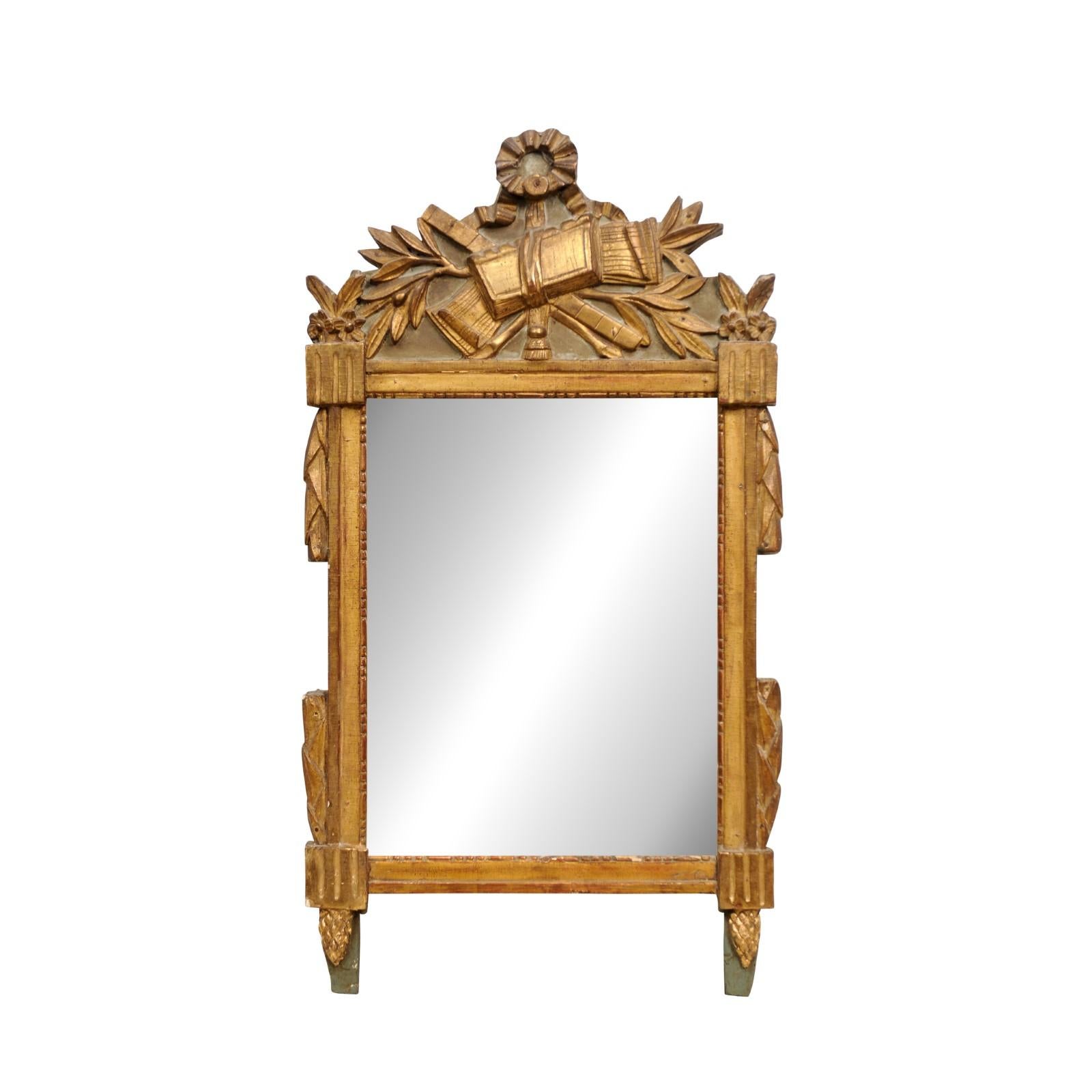 French Louis XVI period giltwood mirror circa 1790 with carved ribbon-tied liberal arts allegory, laurel leaves and pine cone motifs, painted background, slightly aged mirror and rustic character. Introducing a magnificent French Louis XVI period