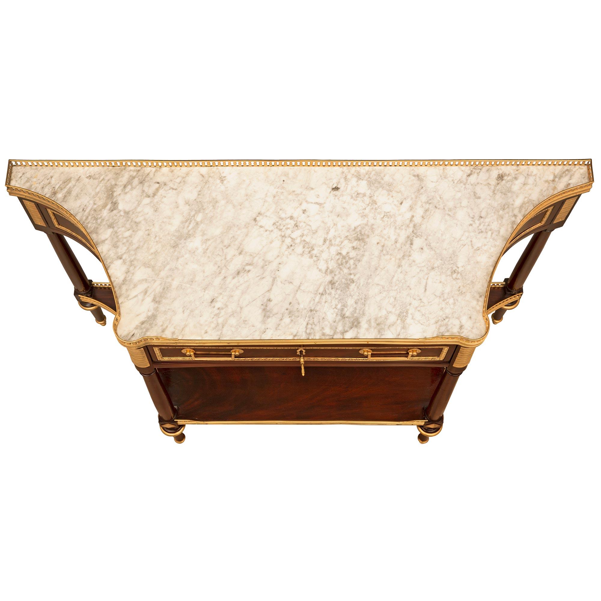 An exceptional French 18th century Louis XVI period Mahogany, ormolu, and white Carrara marble console. The freestanding two tiered console is raised by elegant circular tapered legs with fine ball and topie shaped sabots with mottled top caps below