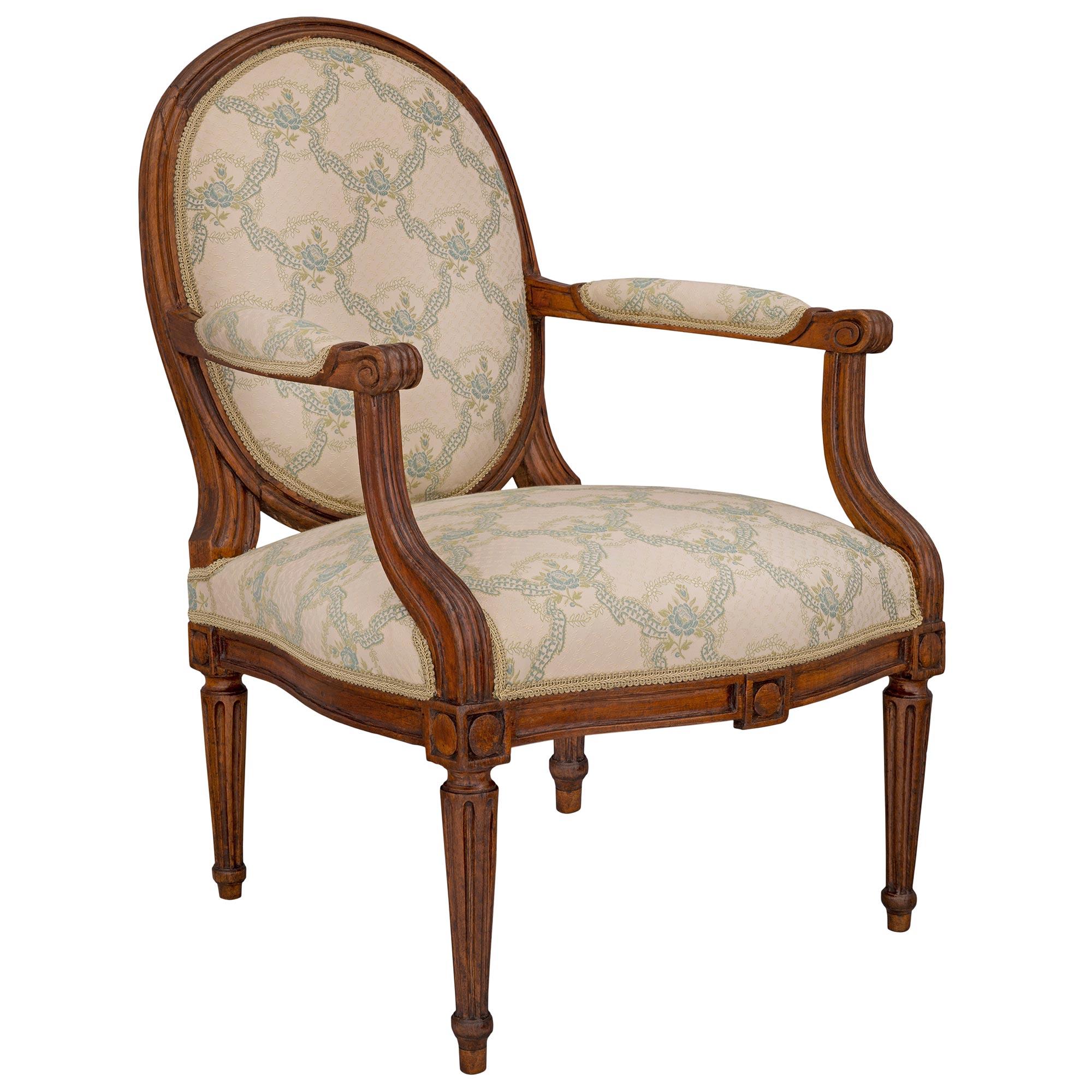 A very attractive French 18th century Louis XVI period walnut armchair, circa 1760. The low seating armchair is raised by elegant circular tapered fluted legs with finely carved block reserves above each leg and at the center of the straight frieze.