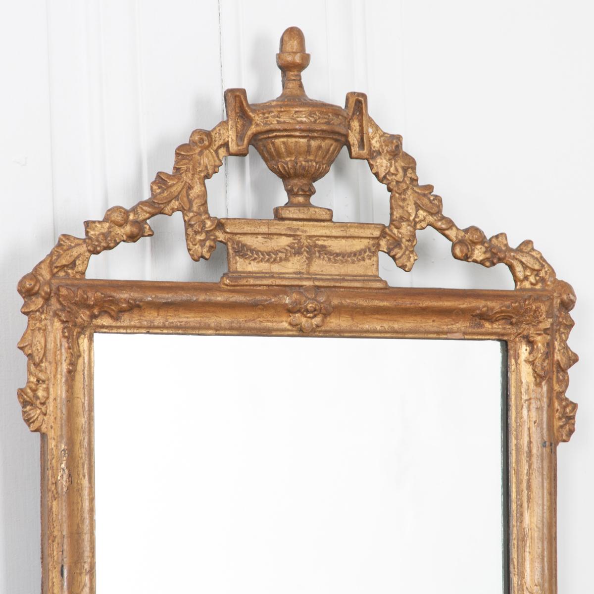 Beautifully hand-carved, this giltwood mirror is overflowing with detail. A carved urn with floral garland triangulates the top of the frame and drapes below the bottom. Each corner of the frame is carved with floral ornamentation. Recently updated