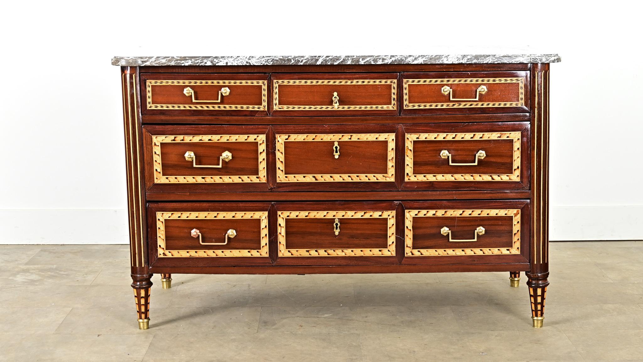 Una straordinaria commode francese in mogano del XVIII secolo, periodo Luigi XVI, decorata con un'impressionante tecnica di intarsio che crea movimento e definizione sui frontali dei cassetti e sui pannelli laterali. Il mobile conserva la lastra