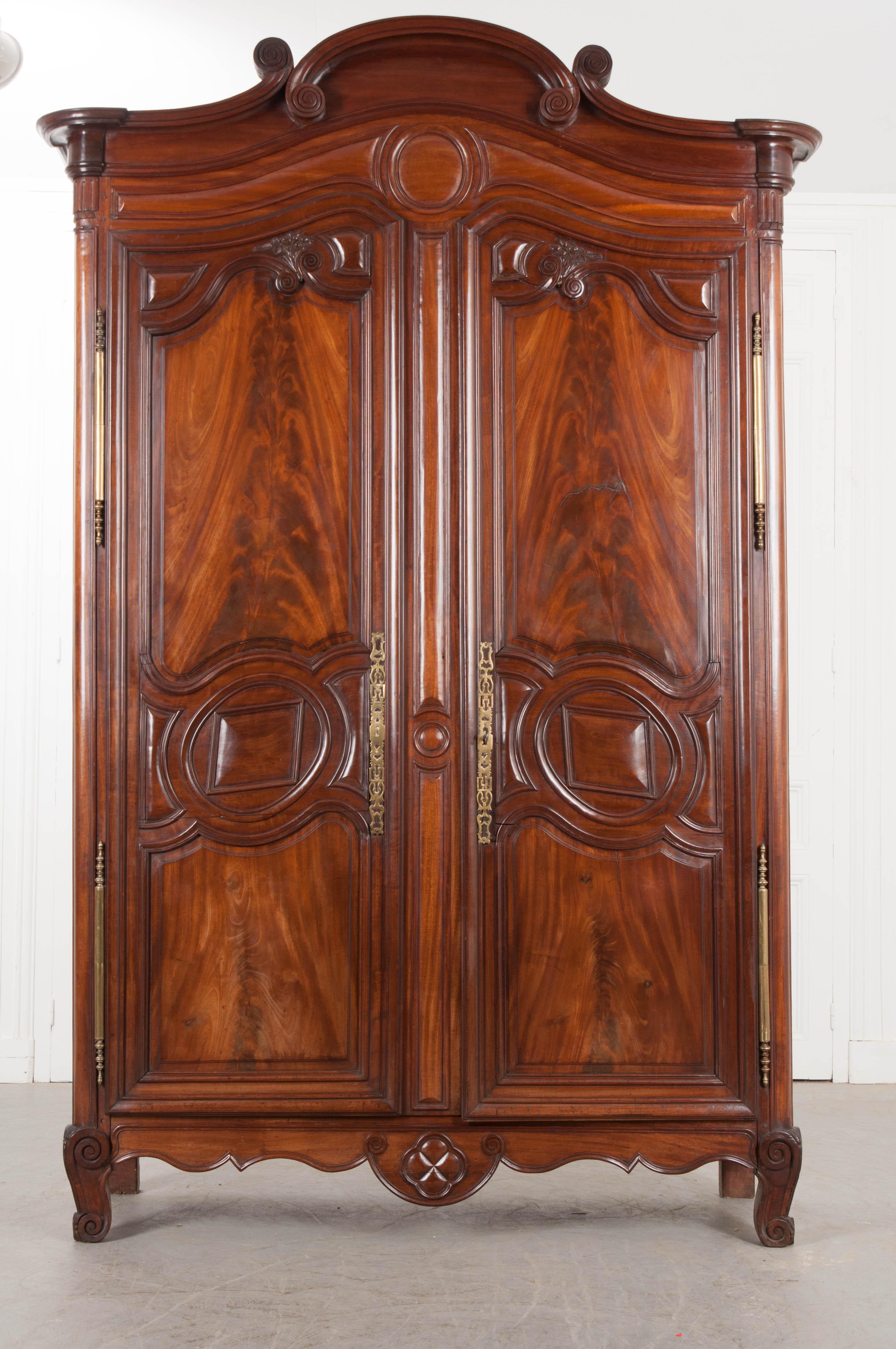 A gorgeous solid mahogany armoire, from the port of Normandy, France, circa 1780. This beautiful antique case piece was hand carved from solid mahogany and is styled with intricately carved scrolled and geometric details. The top is shaped and