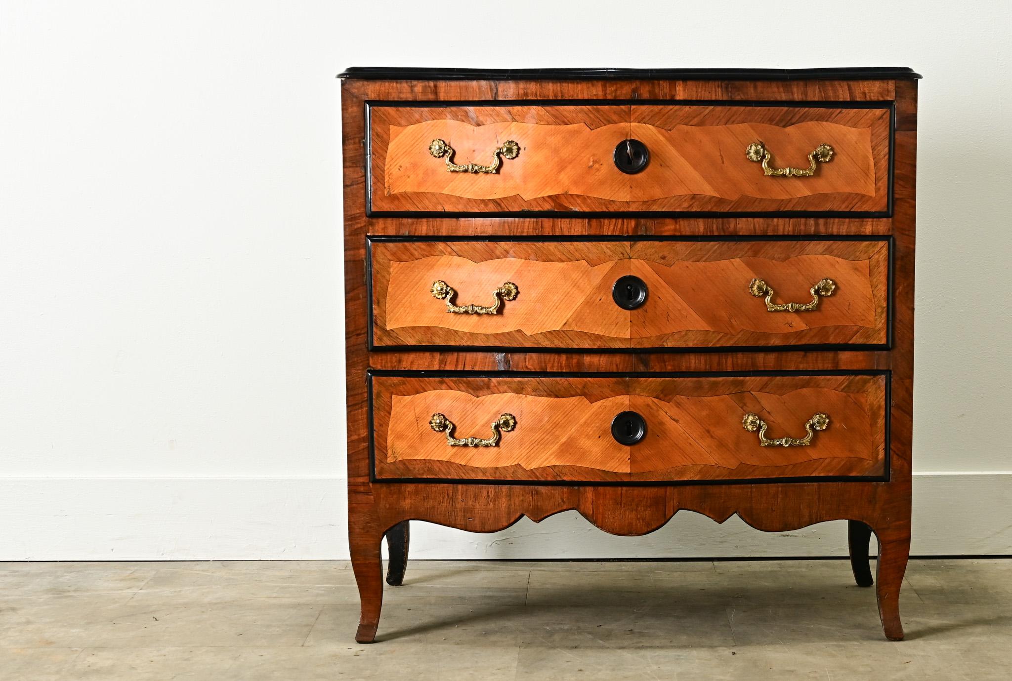 A petite and impressive French marquetry commode from the 1700’s. The commodes top is in wonderful antique condition with marquetry designs trimmed with ebonized molding. There are three drawers all with patterned marquetry designs, gilt bronze