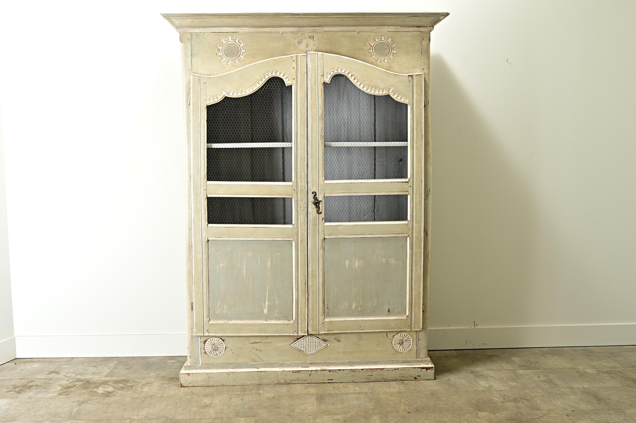 A painted and carved French armoire from the late 1700’s. The cabinet has its original paint finish that is worn in all the right places with whimsical and geographic carved designs. The pair of paneled doors are inset with a worn brass wire and