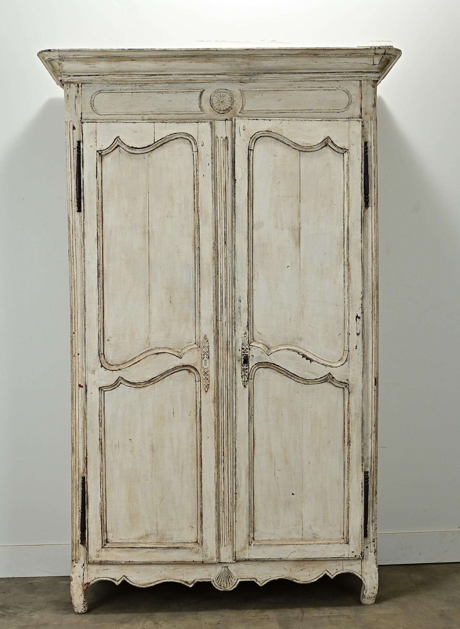 A French Louis XV painted armoire from the early 1700’s. This armoire is paneled and carved on all three sides in the Louis XV style with its original paint finish. A pair of tall doors open with a functioning lock and key to a large interior fitted