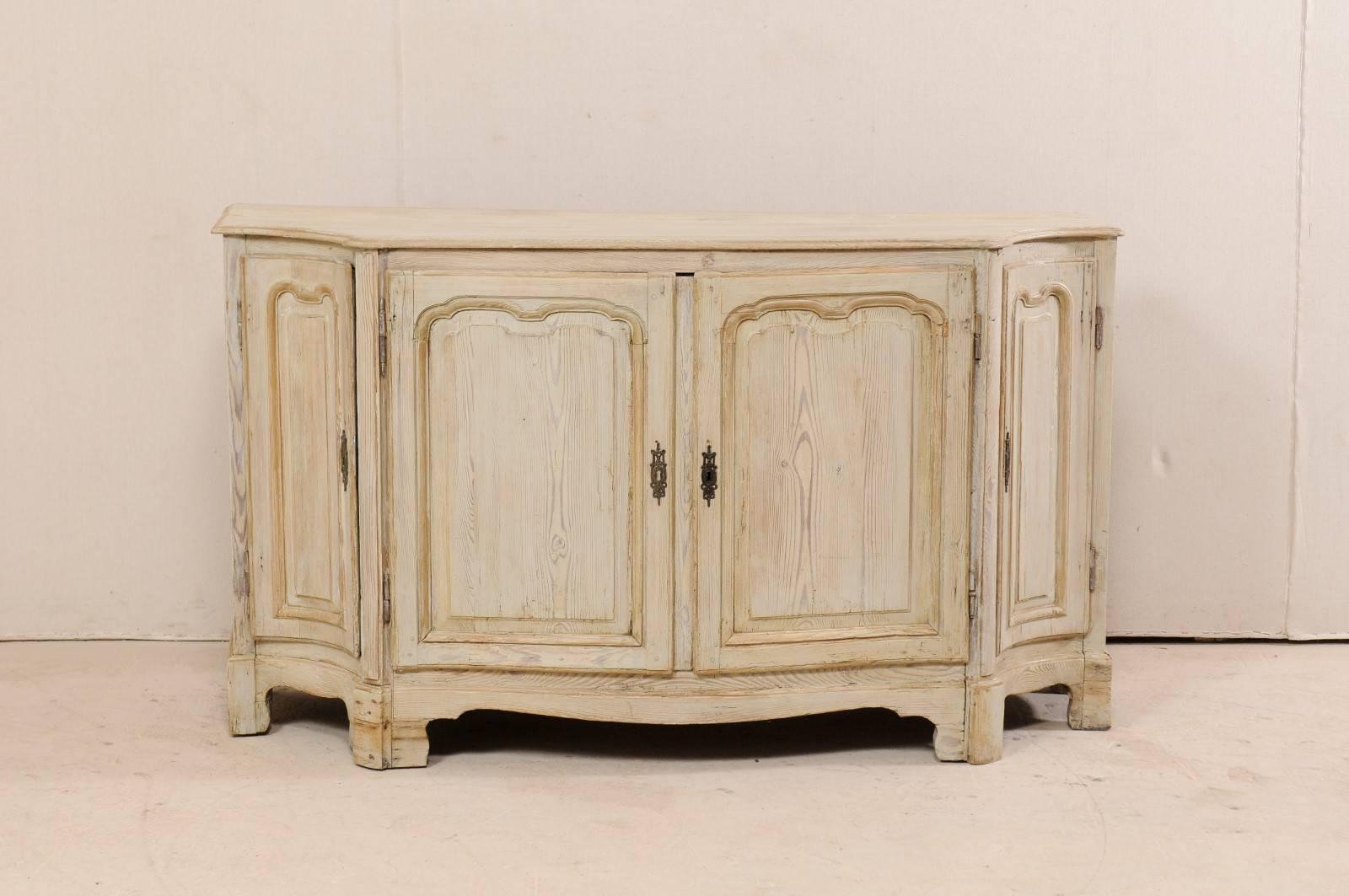 An 18th century French wooden buffet console. This antique buffet cabinet from France features a beautifully fluid design along its scalloped front with concavely shaped, canted sides. There are four drawers, all designed and set seamlessly within