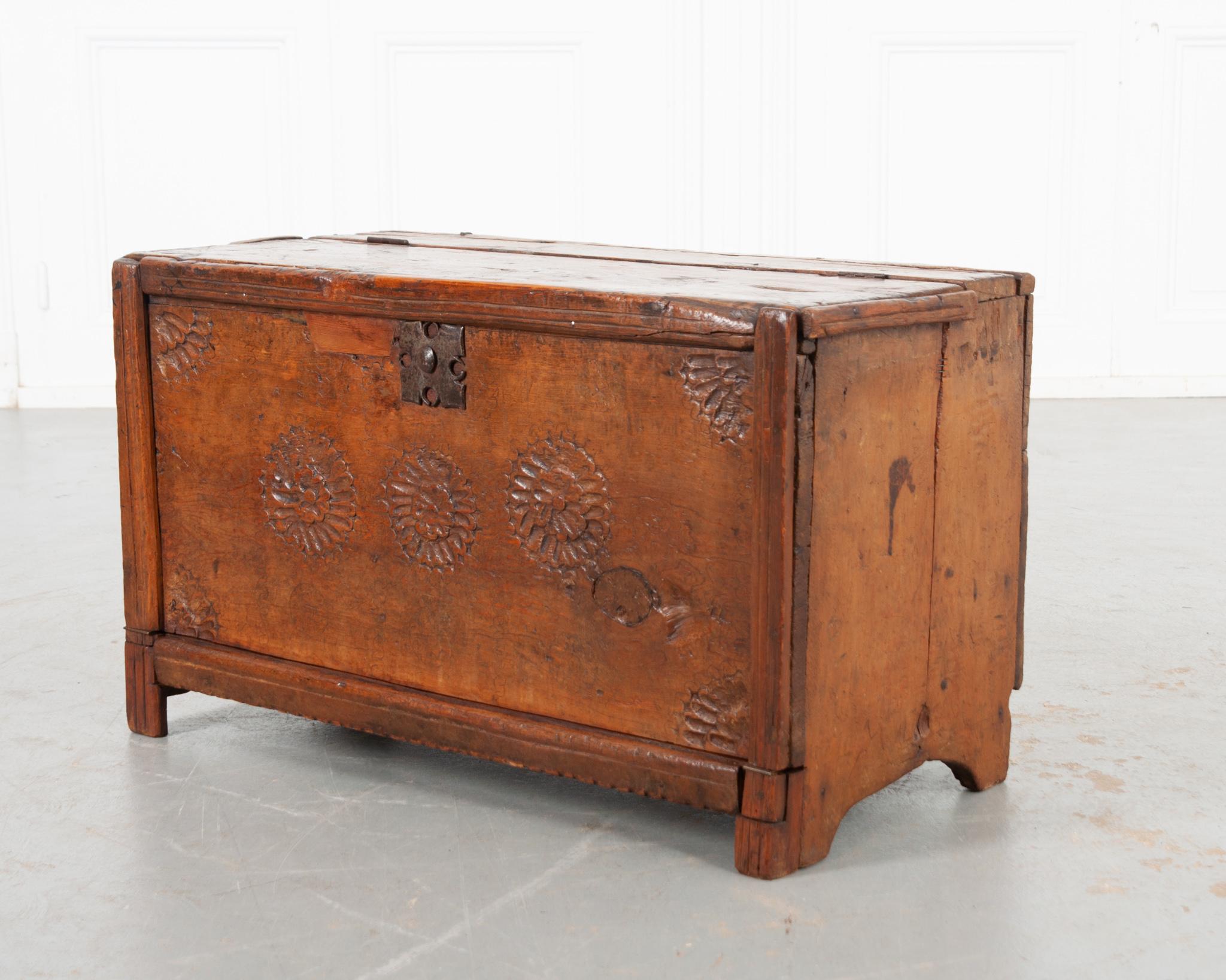 A petite oak coffer from France, circa 1780. Made of solid oak with a rich patina, hand carved flowers and a metal plaque grace the front. The top and front panel open to reveal the interior storage cavity. After nearly 250 years of use it’s is good