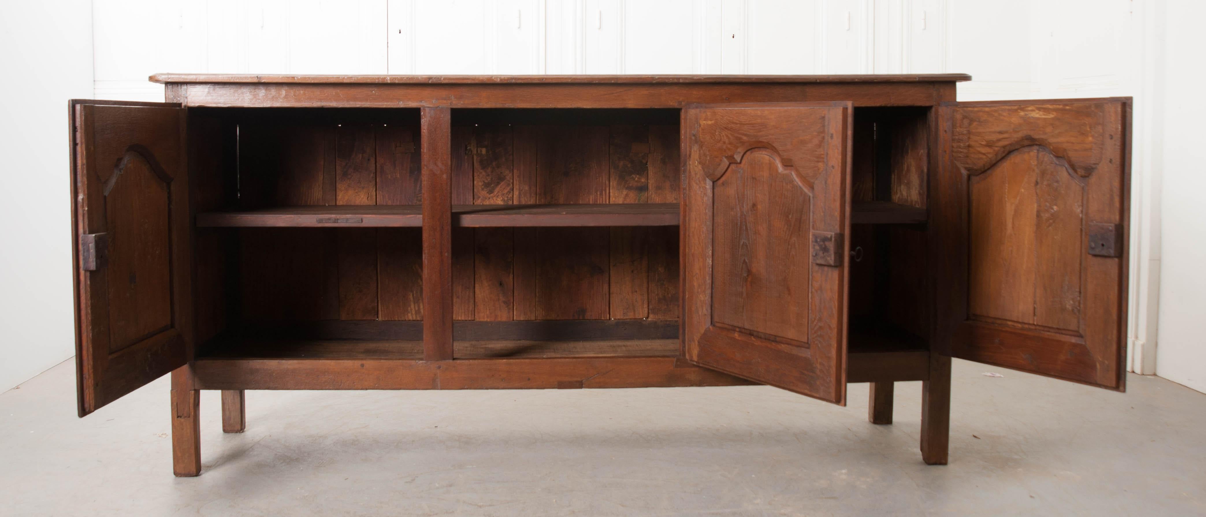 This handsome carved French enfilade, circa 1750, was found in the Provincial countryside and constructed of solid walnut and chestnut. The carved top rests above three doors, with shaped panels, which open to reveal a single fixed shelf, and the