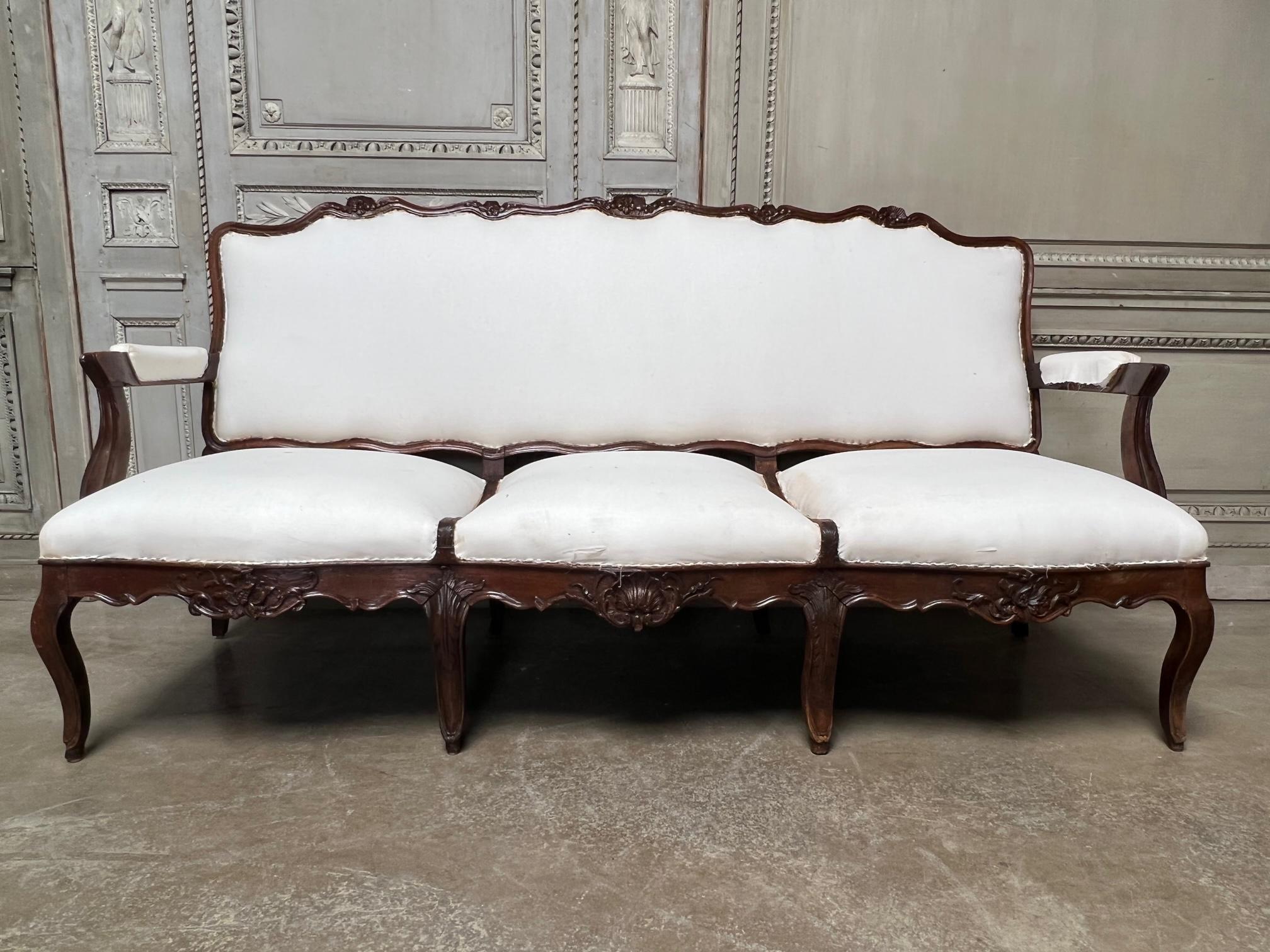 A large French Regence carved walnut canape, sofa with cabriole legs and carved shell andnfoliage. This sofa is in a late Regence period with hints of Louis XV style assymetry This unusual sofa has carved walnut separating the seat into three