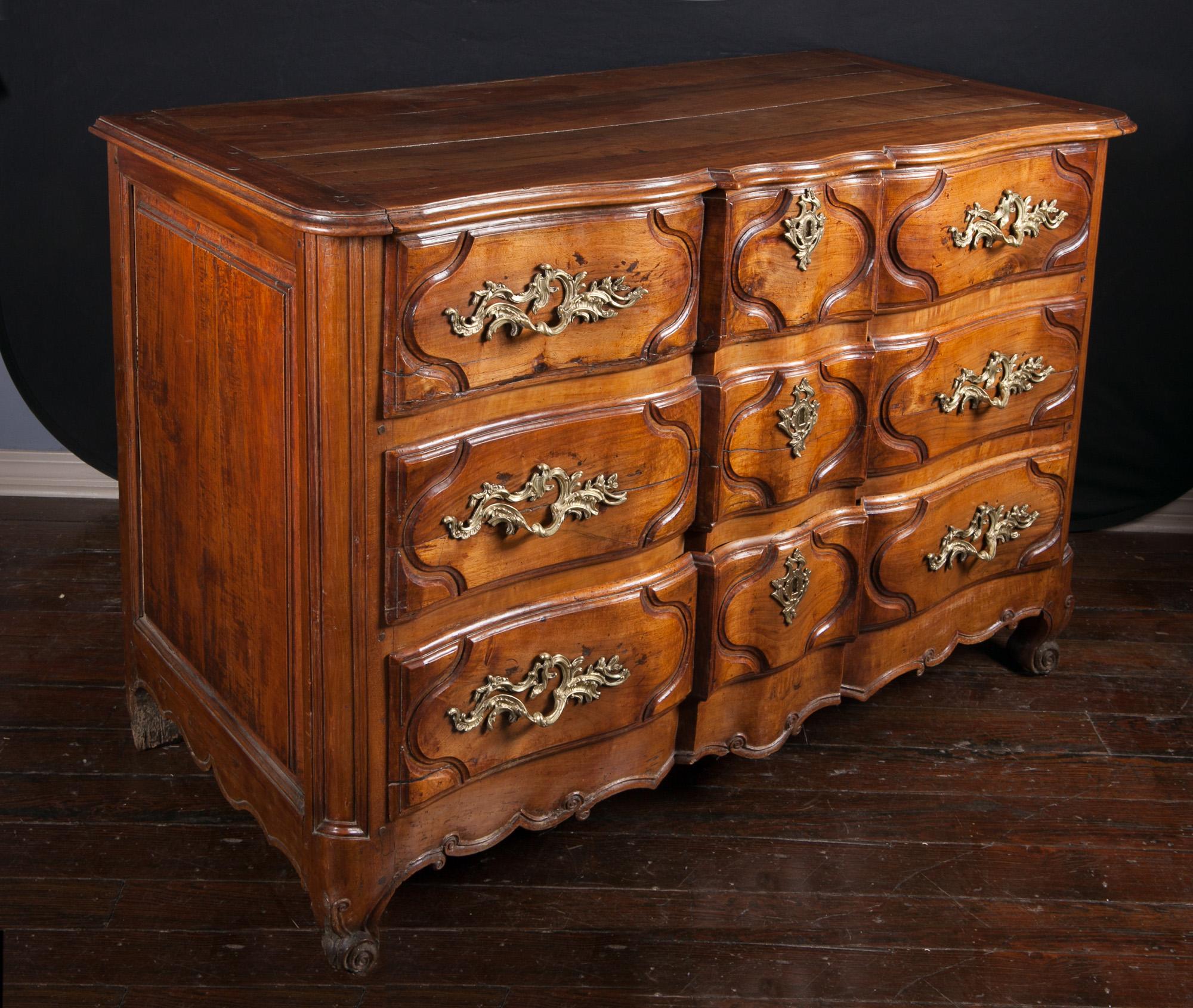 This 18th century Lyonnaise commode is simply exquisite. The piece is made of walnut in the Regence in style and features three drawers, all with the original bronze d’ore handles and escutcheons. The walnut top is contoured beautifully, and the