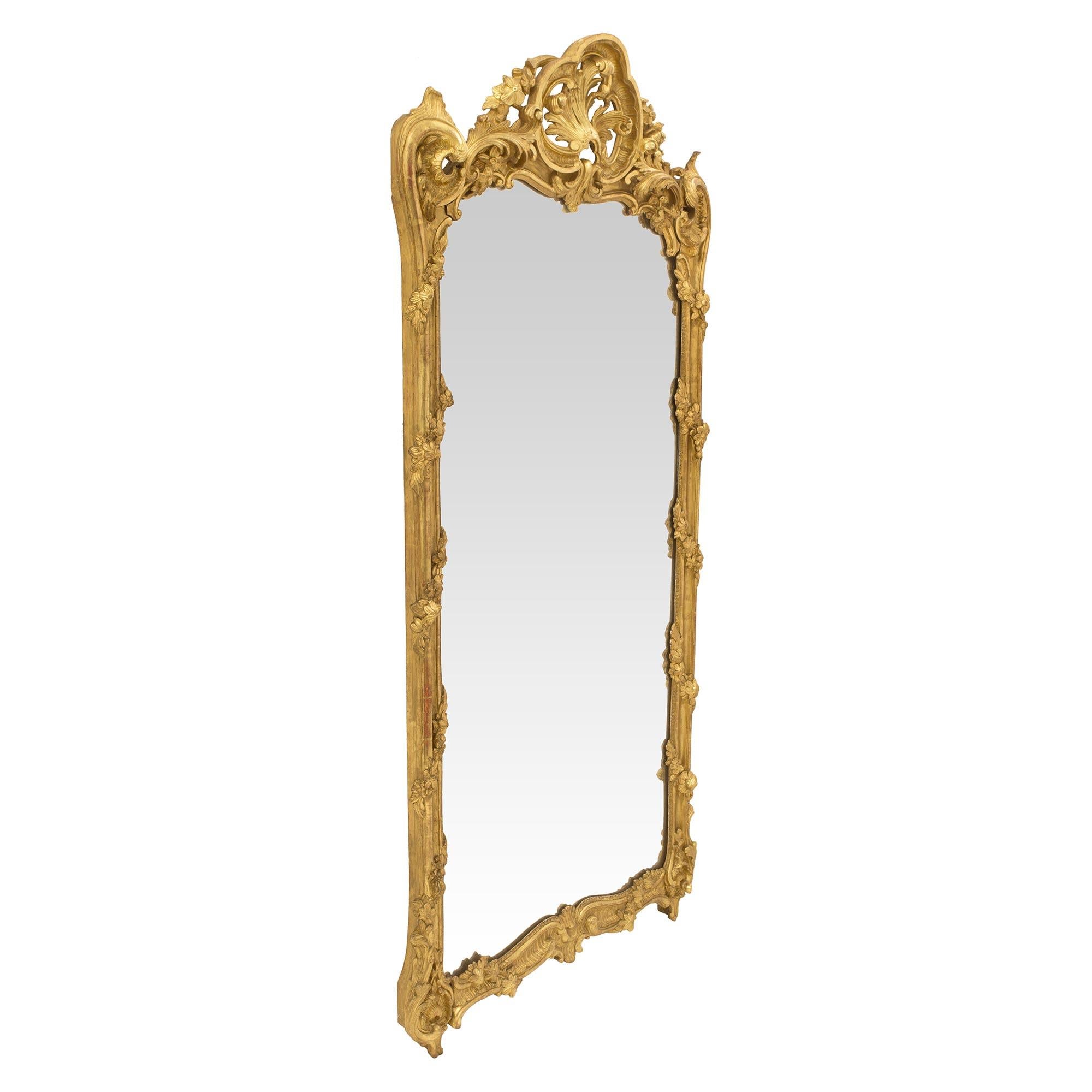 Un étonnant et grand miroir en bois doré de la période Régence du 18ème siècle. La plaque de miroir d'origine est encadrée d'une belle et très décorative bordure mouchetée avec de charmantes guirlandes florales enroulées finement sculptées. La base