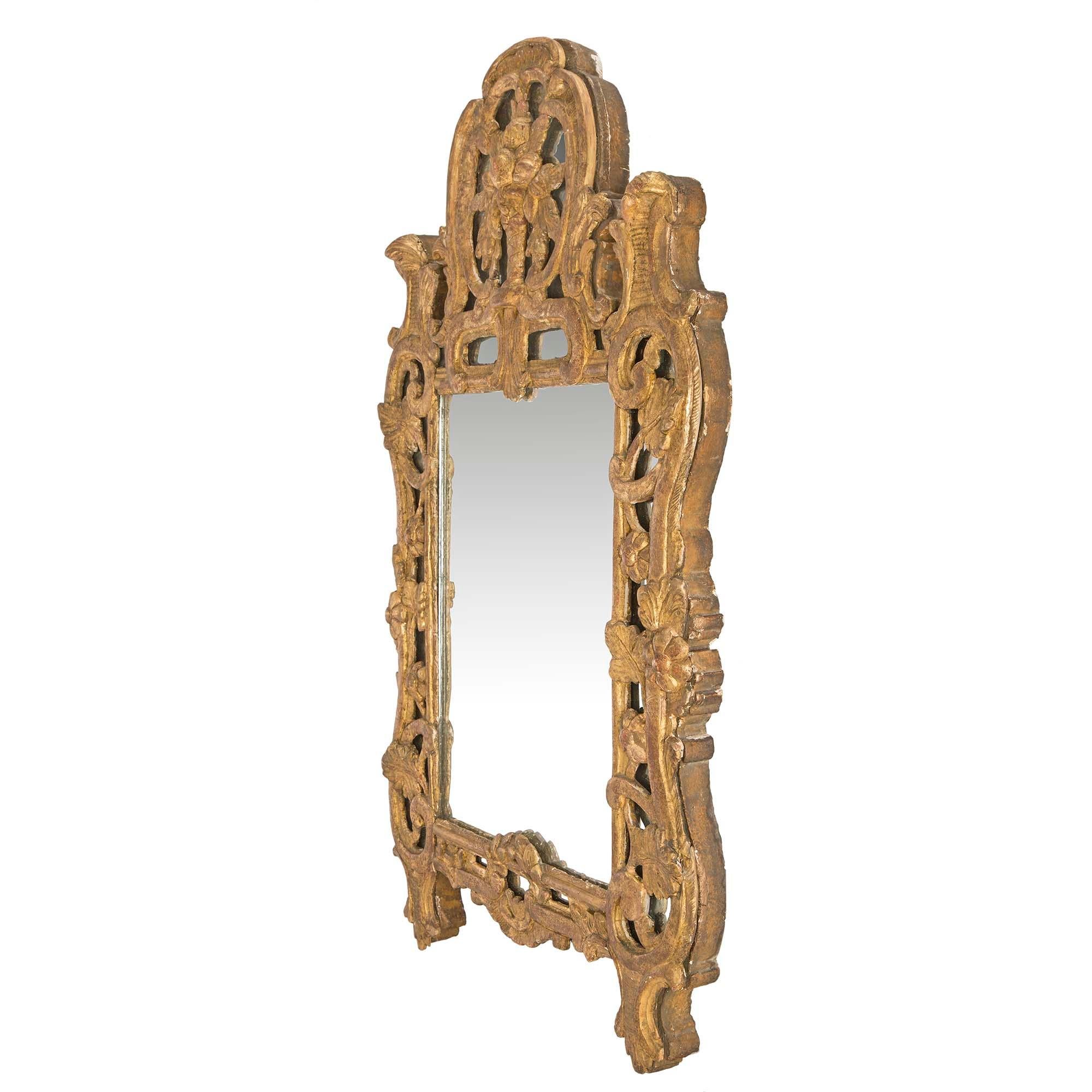 A smaller scale striking French 18th century Régence period giltwood mirror. This handsome mirror has a pierced scrolled giltwood frame adorned with all original mirror plates. Centered at the bottom is a laurel wreath and scrolls continue up each