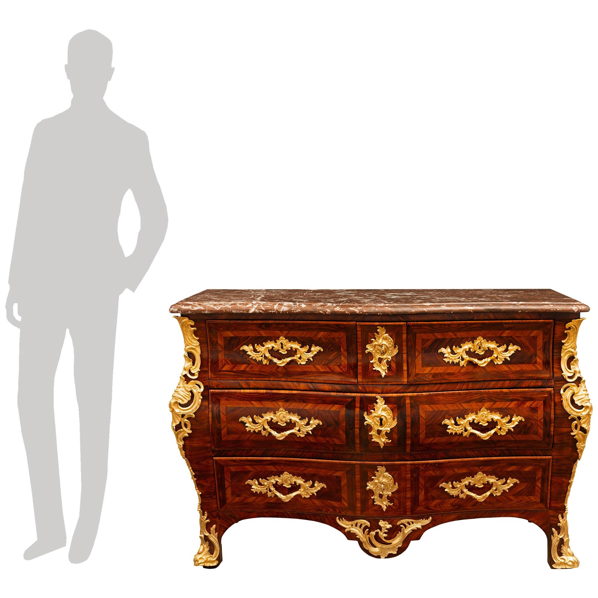 Una splendida e decoratissima commode Tombeau francese del periodo Régence del XVIII secolo, in legno di quercia, Ormolu e marmo Rouge Royale. Questa imponente commode a cinque cassetti è sollevata da eleganti piedi curvi con sabot in Ormolu