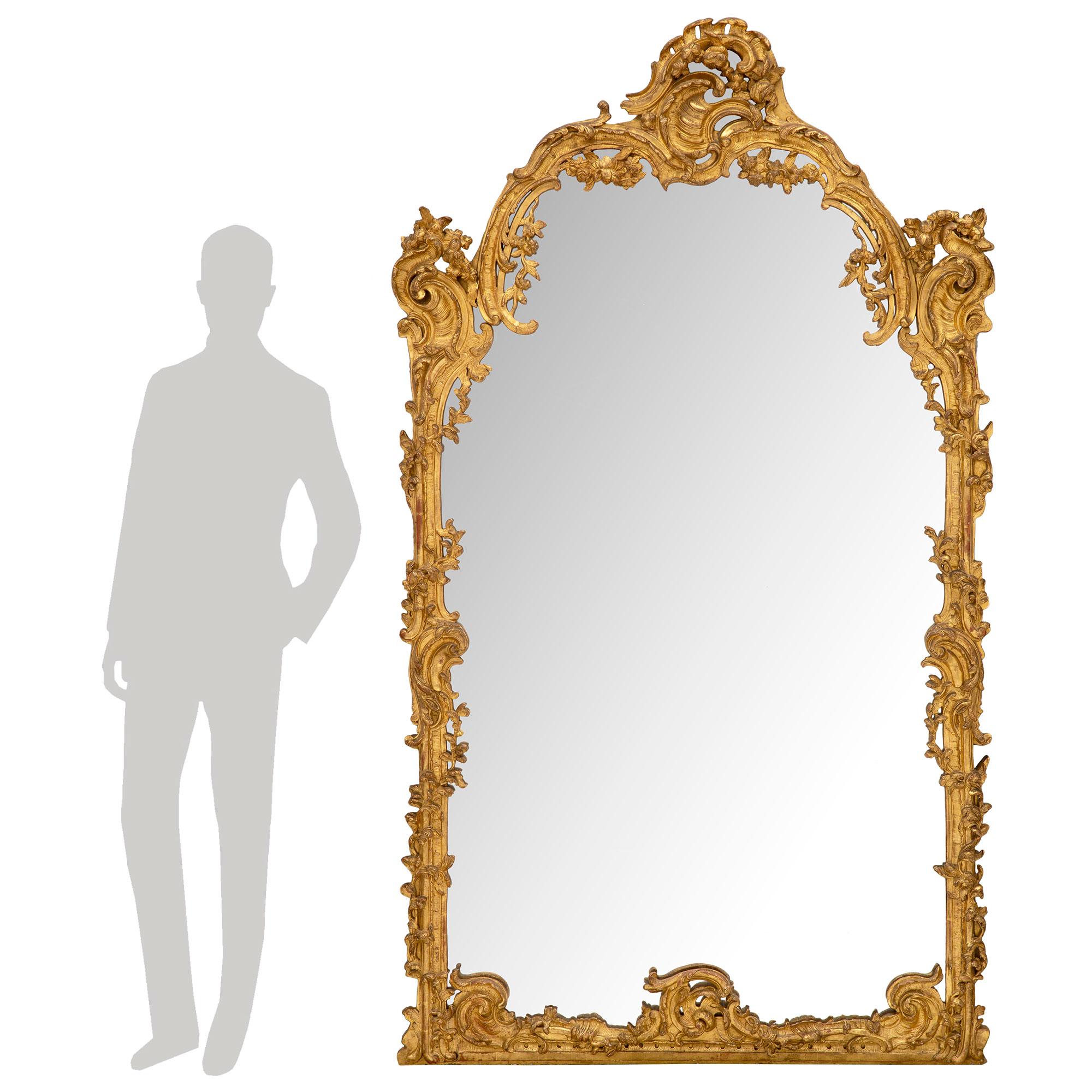 Superbe et grand miroir en bois doré de style Régence du XVIIIe siècle. La plaque de miroir d'origine est encadrée d'une étonnante bordure mouchetée richement sculptée, avec des mouvements de feuillage enveloppants très détaillés. La base droite est