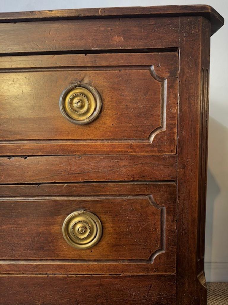 Questa splendida commode francese del XVIII secolo è realizzata in legno di ciliegio, presenta due cassetti, quattro gambe affusolate decorate con scanalature e maniglie in ottone con anelli.