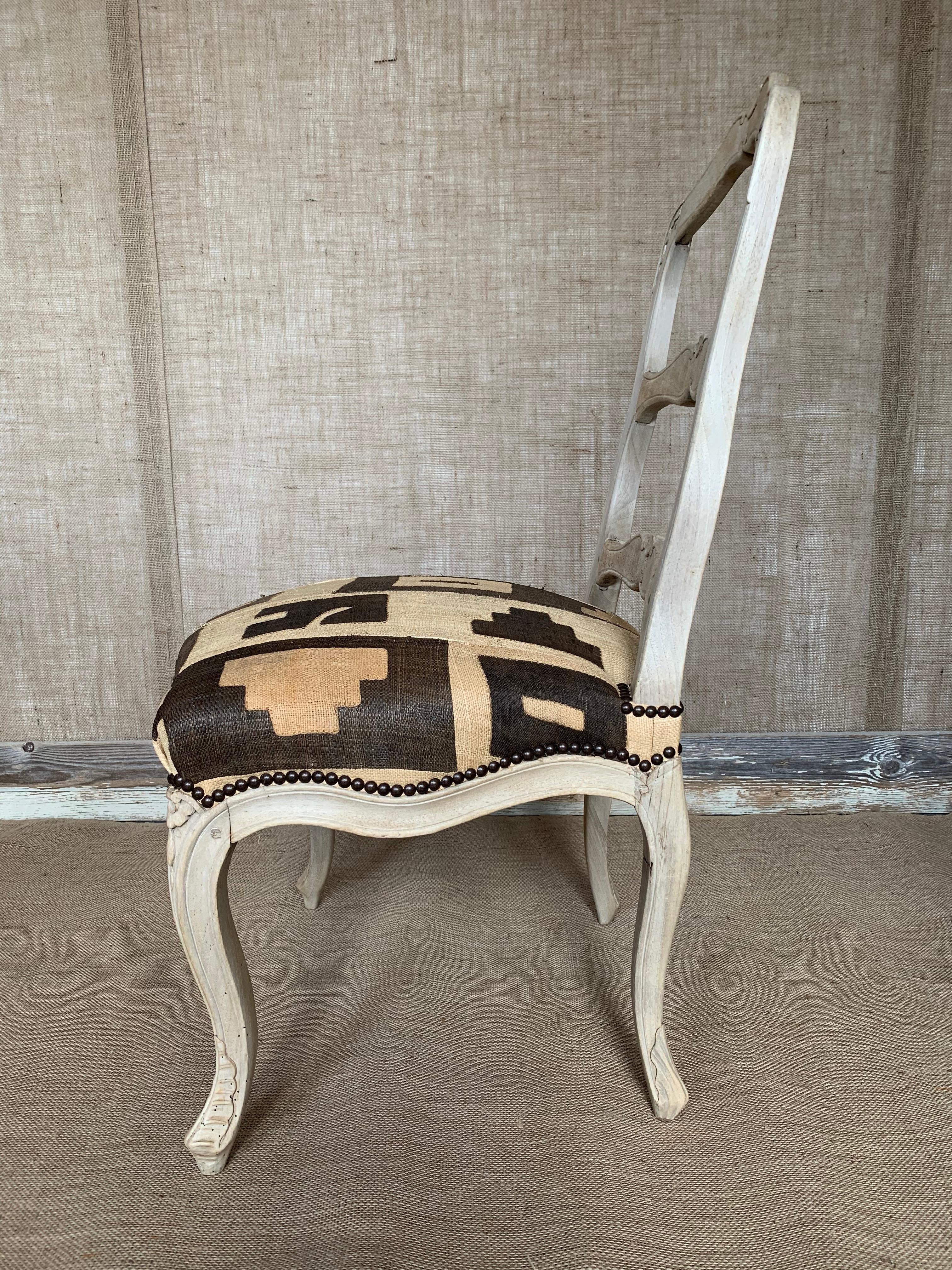 A French 18th century Louis XV side chair in bleached walnut, with an open ladder back and carved crest rail, above an upholstered seat cushion in African Kuba cloth, with carved apron and cabriole legs, circa 1760.