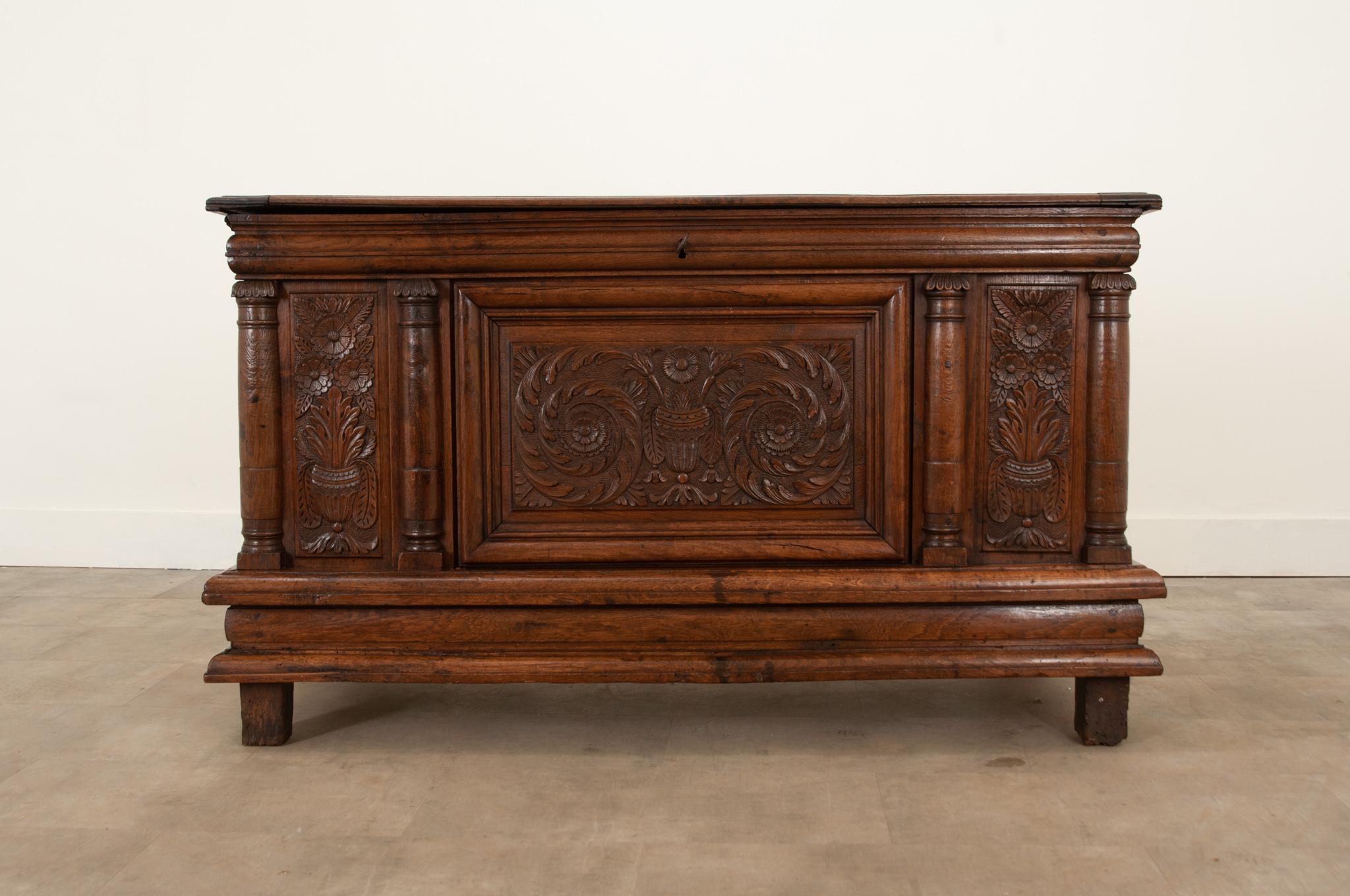 This solid oak coffer from the 1720s is full of gorgeous hand carved details and a wonderful patina. Swirling acanthus leaves and florals beautifully adorn the facade. Four columns break up the front motif. A small candle box with a hinging top is