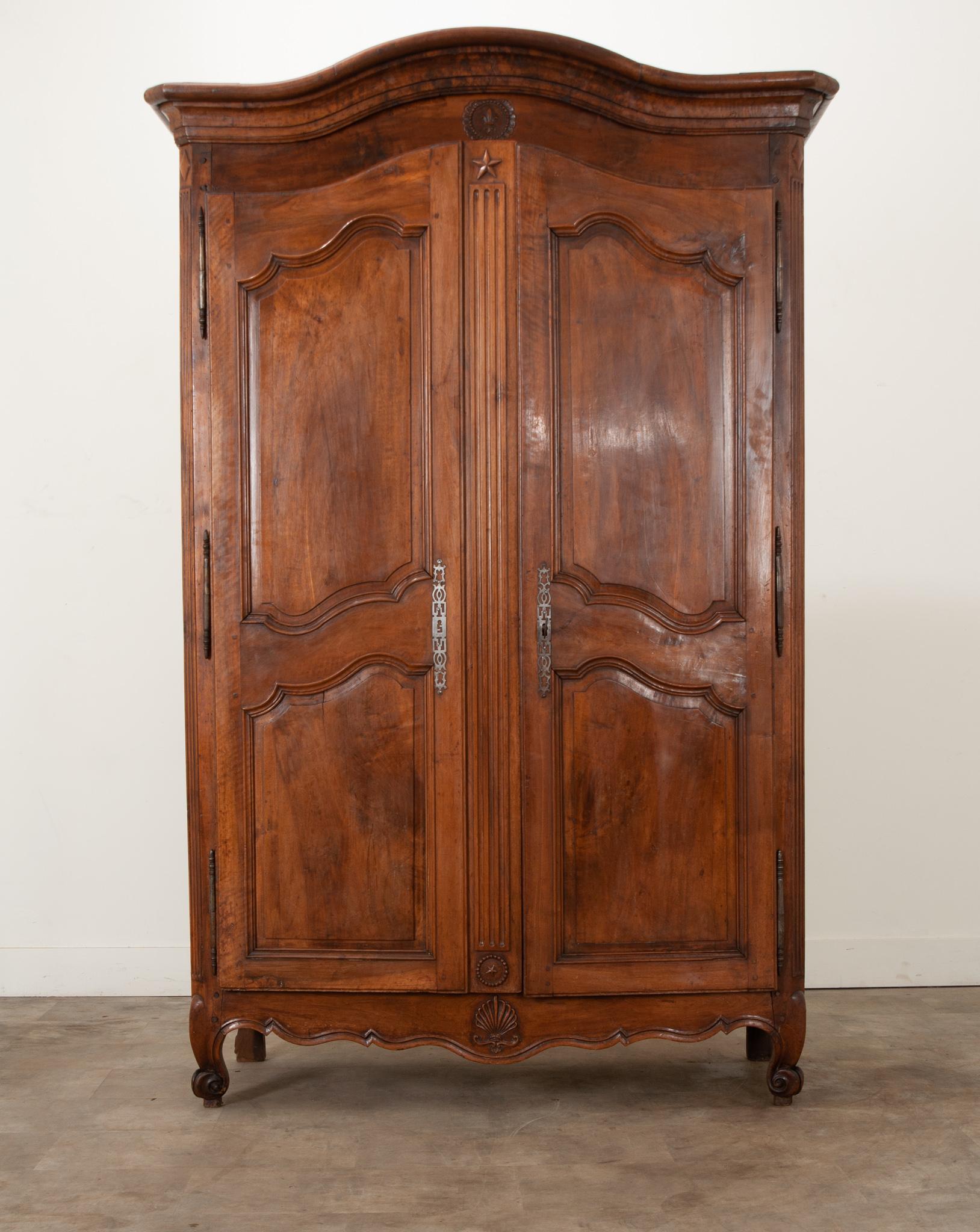 A French carved, solid walnut armoire built in the Louis XV period. A Chapeau de Gendarme cornice tops the body of the armoire. Two solid walnut doors have shapely carved panels creating a gorgeous façade with style-matching, recessed panels. The