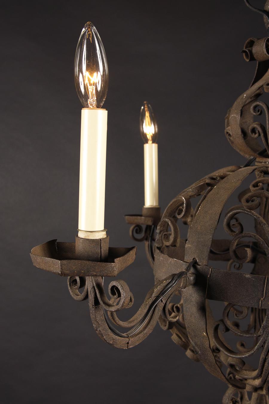 This 18th century spherical chandelier is made from hand wrought iron circa 1780. The French antique piece features iron bobeches and floriate scroll decorations at top, with a floriate finial. It’s classically medieval in design and draped in