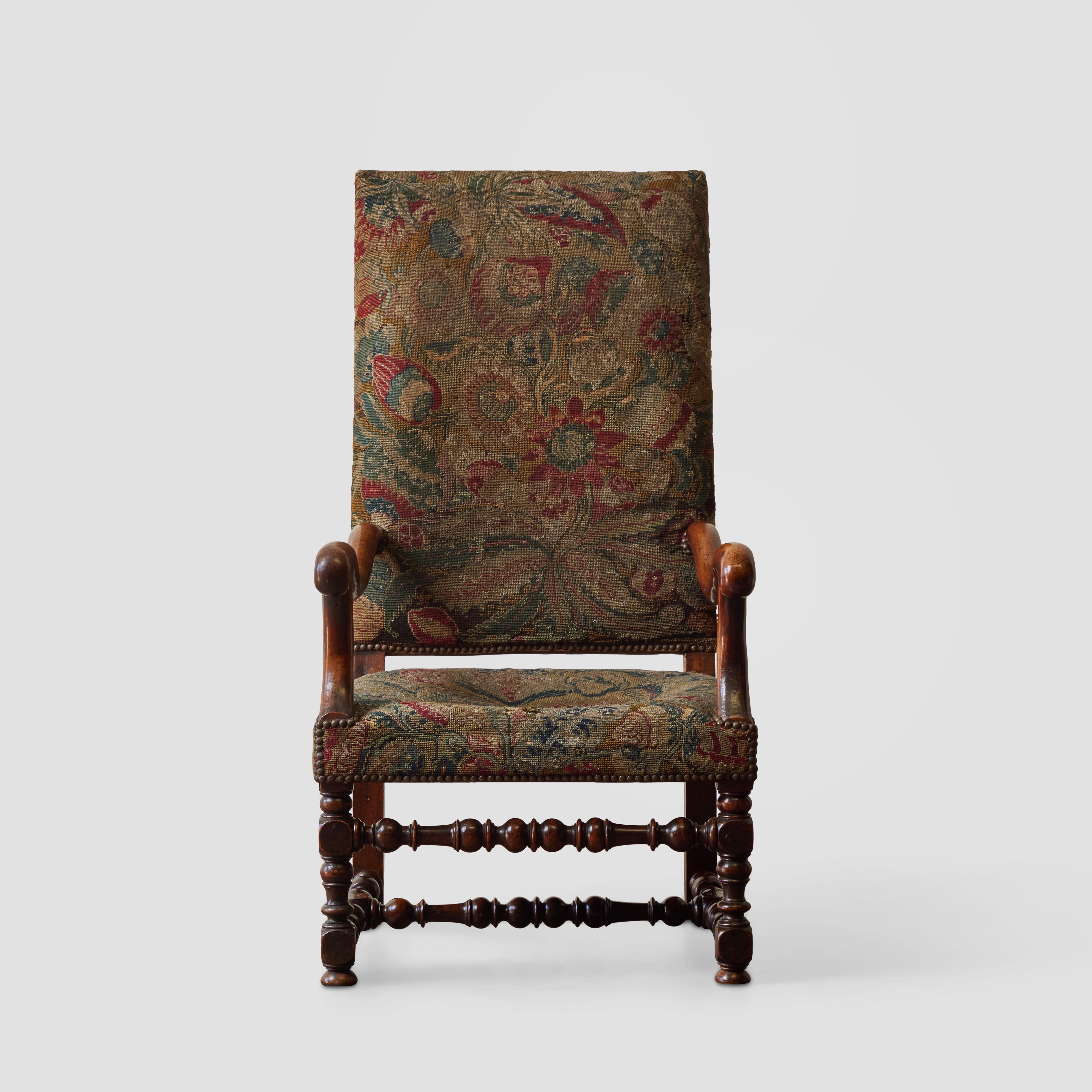 Exquisite French 18th-century high-back armchair with original handwoven tapestry upholstery and turned wood legs. This piece is exceptional for its craftsmanship and finely aged condition. With dusky shades of gold, crimson, blue, and moss, the