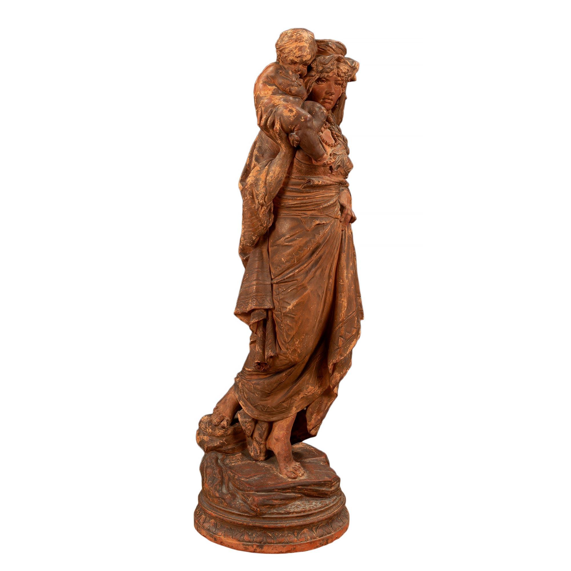 A wonderful French 18th century terra cotta signed statue of mother and child. The statue is raised on a circular terrain designed base. The woman is barefoot donned in a traditional gown with a pearl styled necklace and head dress. the woman is