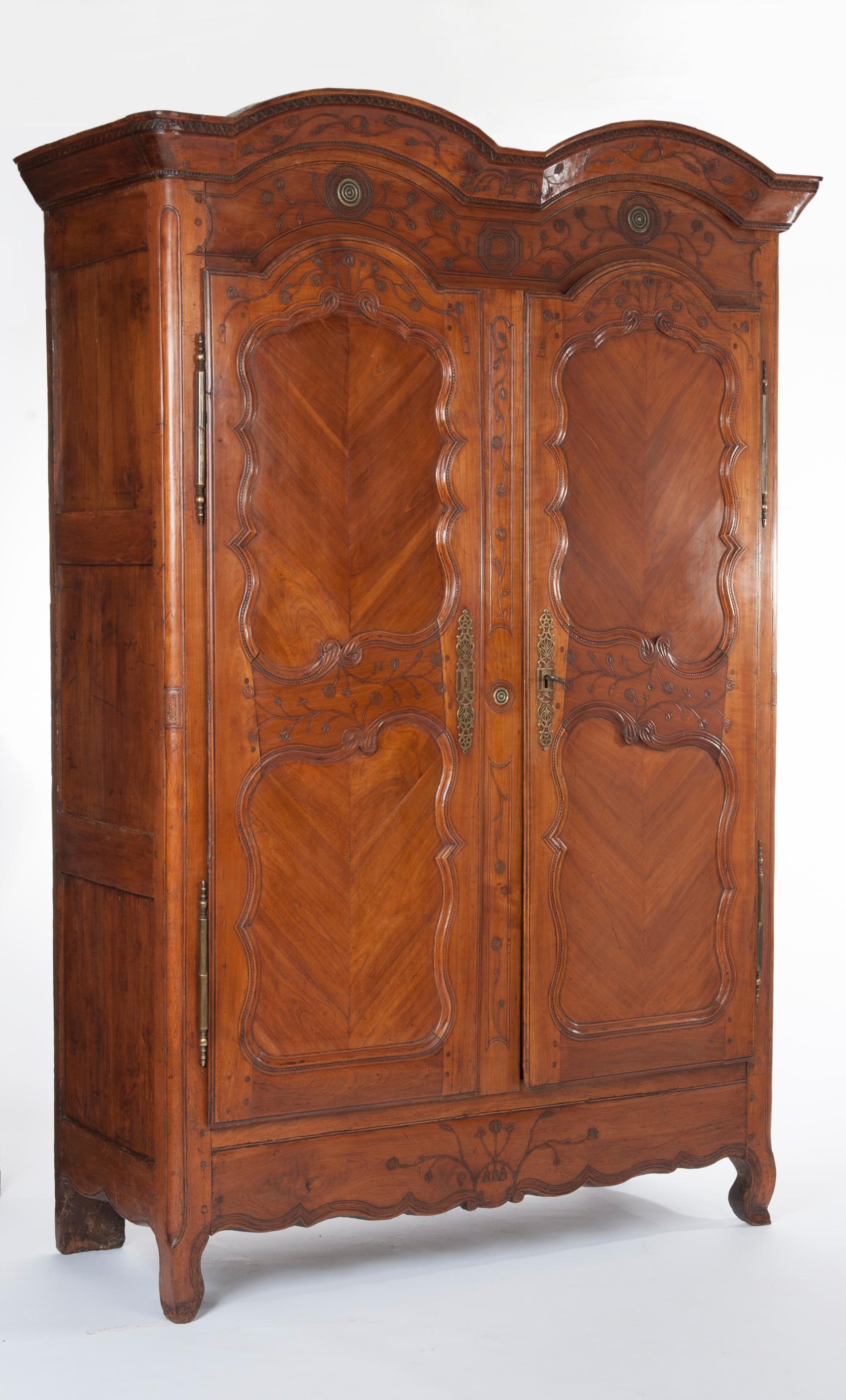 This is a rather beautiful tall French mid-18th century Transition solid cherrywood armoire cupboard with bonnet top (chapeau de gendarme), decorative shaped panels and original brass door furniture and locks. Fitted interior, including three