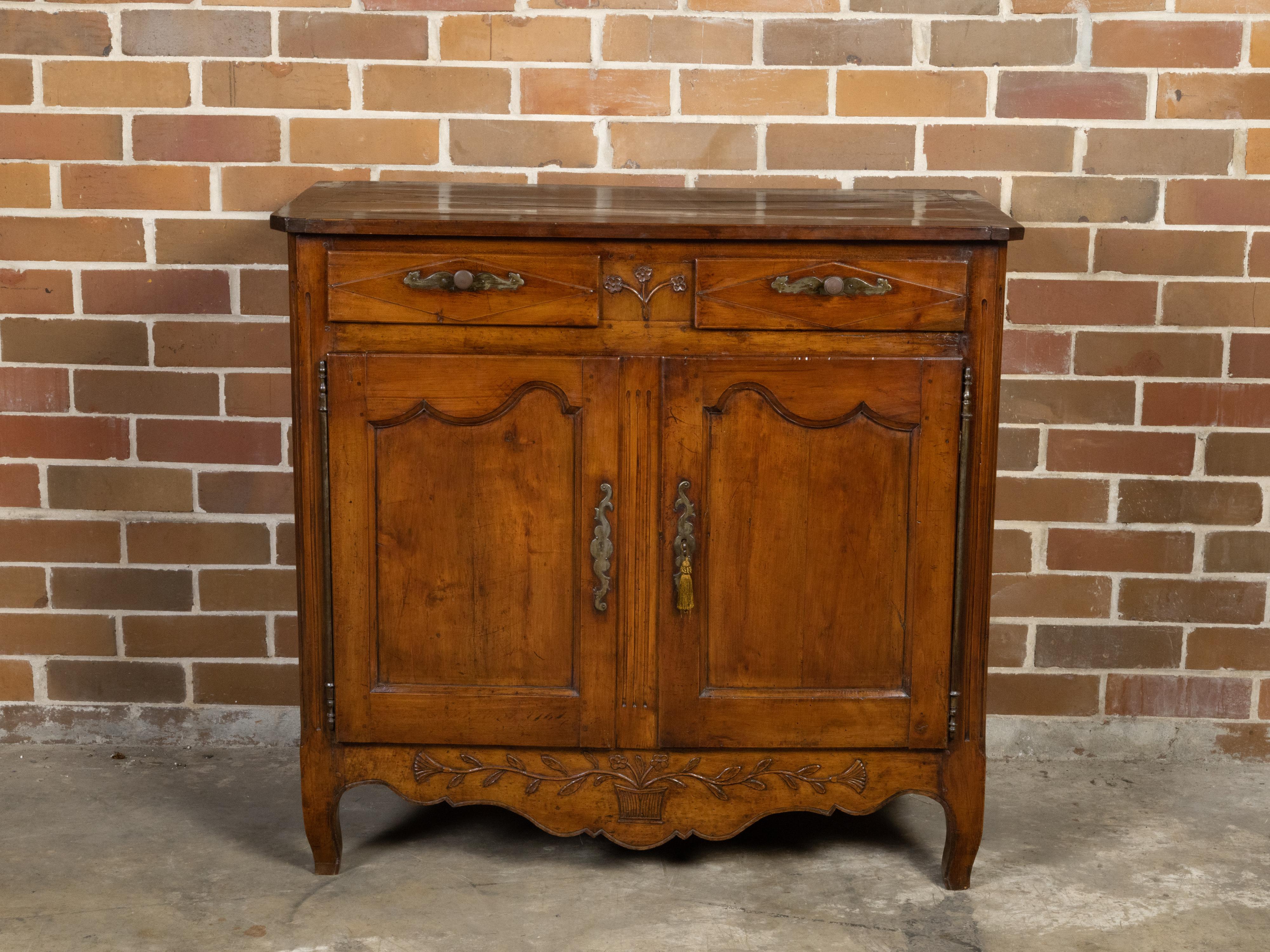 A French walnut buffet from the 18th century, with carved floral motifs, two drawers and two doors. Created in France during the reign of King Louis XV in the 18th century, this walnut buffet features a rectangular top with canted corners in the