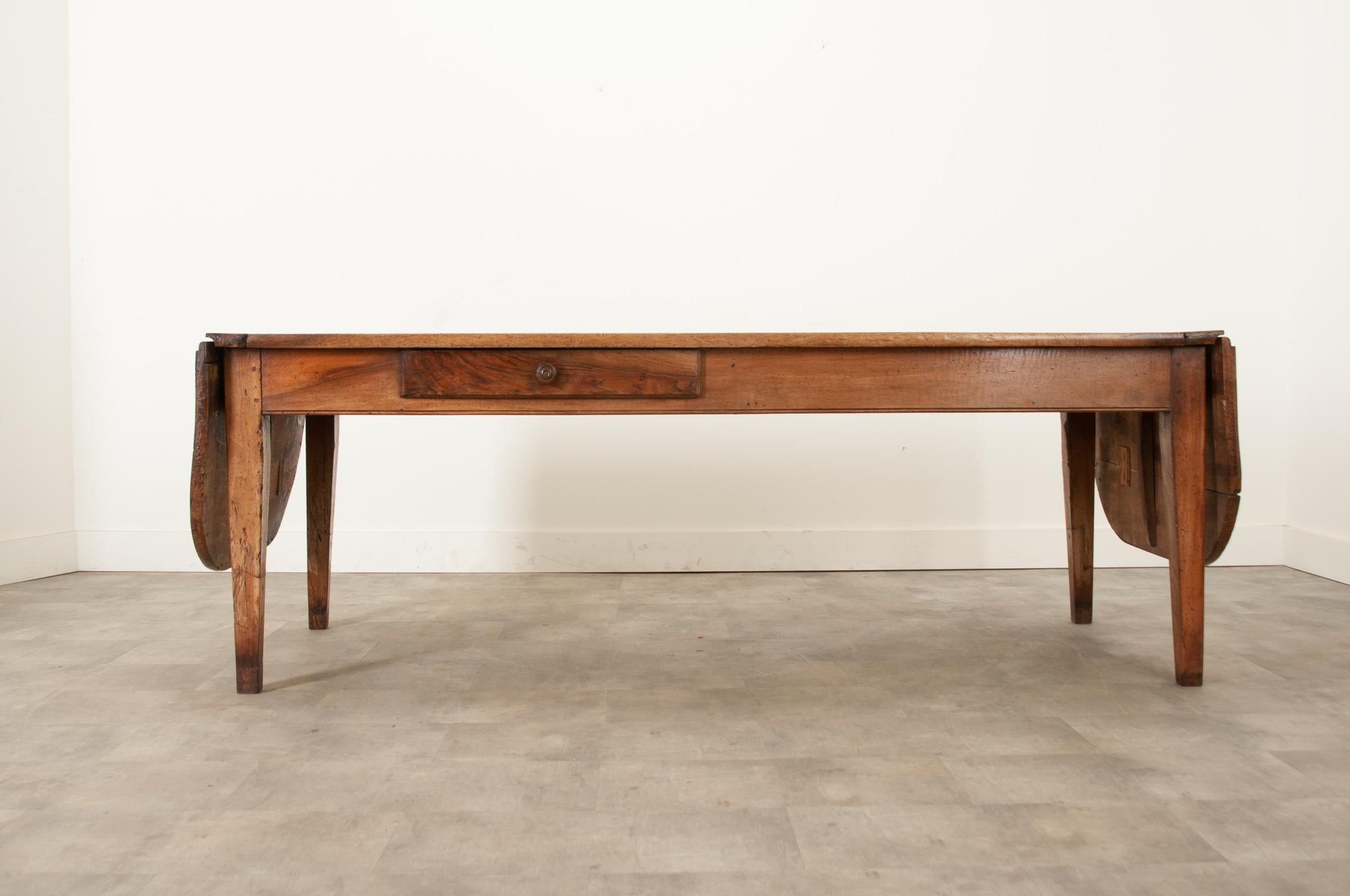 An impressive solid walnut dining table over 10’ long from the 1780’s Normandy, France. This dining table is versatile with two functional drop leaf ends. Recently polished with a French paste wax, this table has a stunning patina that you can’t