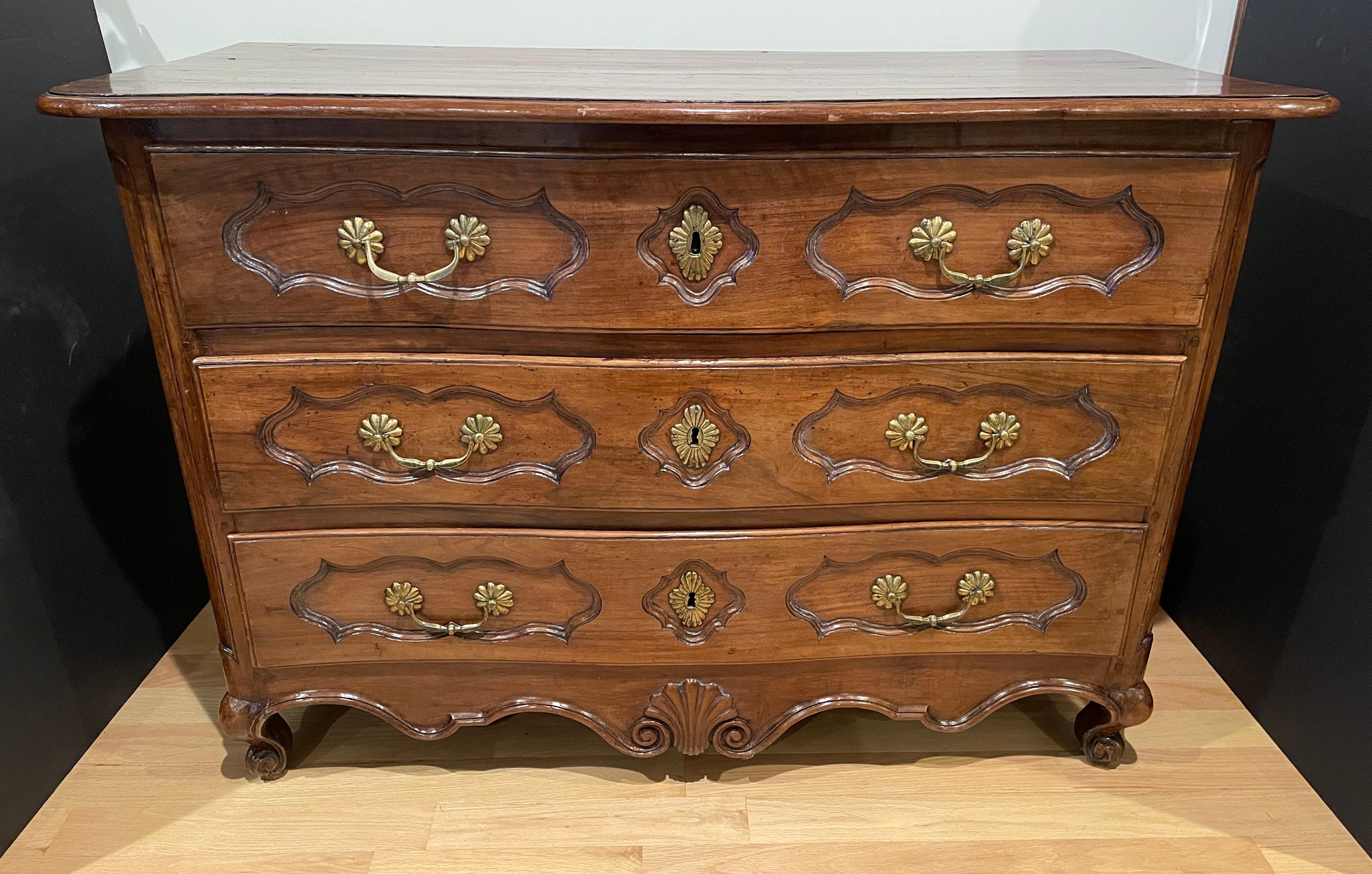 An 18th-century French Louis XV period serpentine-front fruitwood commode chest of three drawers, standing on elegantly carved feet. Distributed over three rows, each moulded drawer is decorated with original handles and escutcheons. Bottom