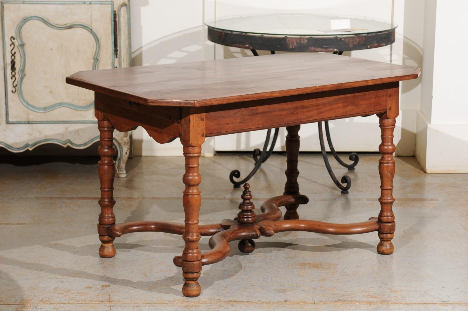 A French walnut side table from the 18th century, with canted corners, lateral drawers, X-form stretcher and carved finial. Born in France during the Age of the Enlightenment, this exquisite walnut side table features a rectangular top with canted