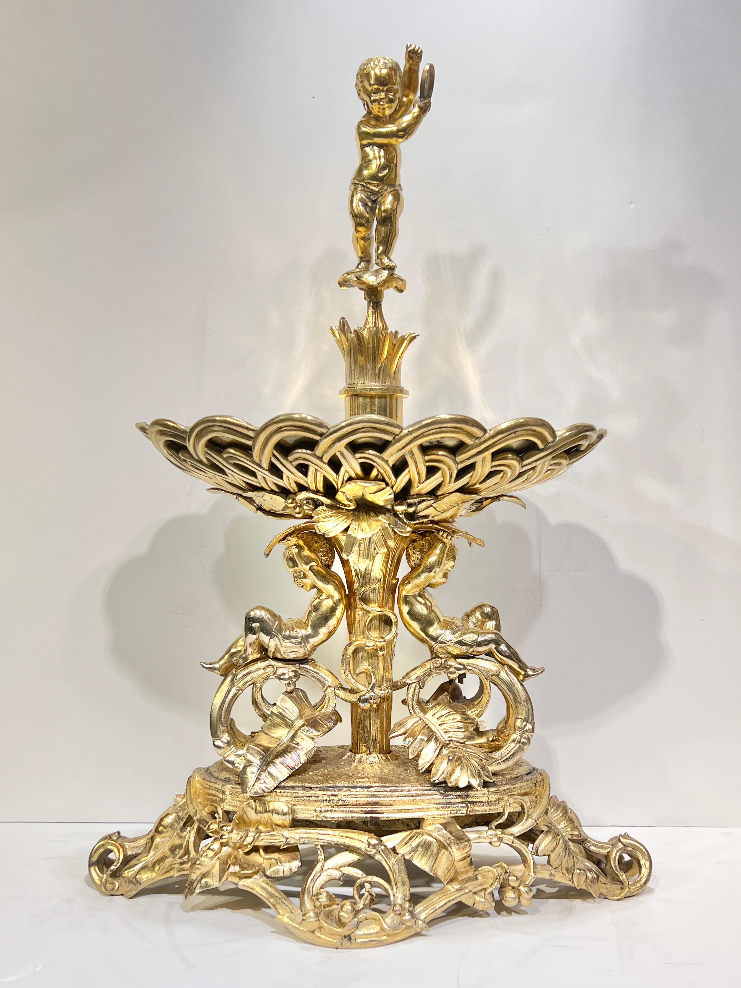 Finest quality Antique (19th century) gilt bronze centerpiece bowl supported by two cherubs among foliate scrolls and surmounted by a cherub holding a tembrel.  26 inches tall, 16 1/2 in wide and 9 1/2 in deep.