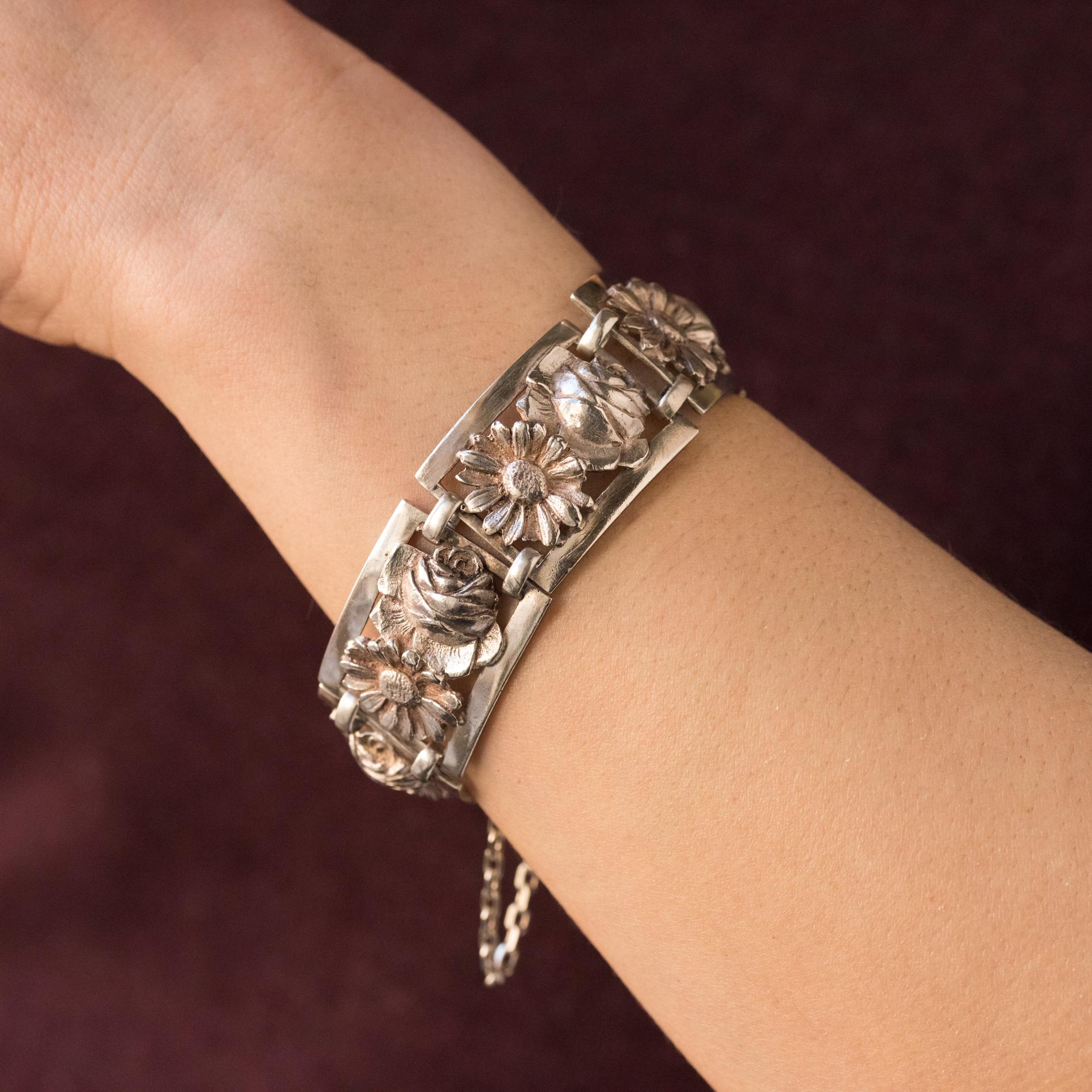 Bracelet en argent, poinçon crabe.
Magnifique bracelet ancien du début du XXe siècle, il se compose de motifs rectangulaires sculptés chacun d'une rose et d'une marguerite et reliés entre eux par deux anneaux oblongs. Le fermoir est un cliquet à