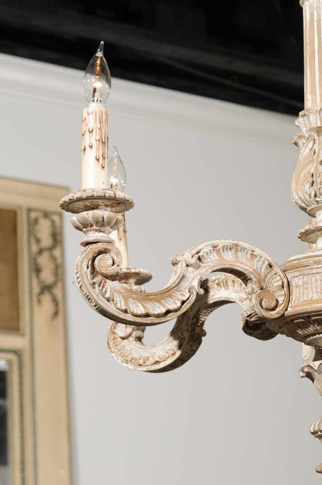 A French carved and painted wood six-light chandelier from the turn of the century, with central column and scrolling arms. Born in France during the late 19th-early 20th century, this exquisite chandelier features a central wooden column adorned