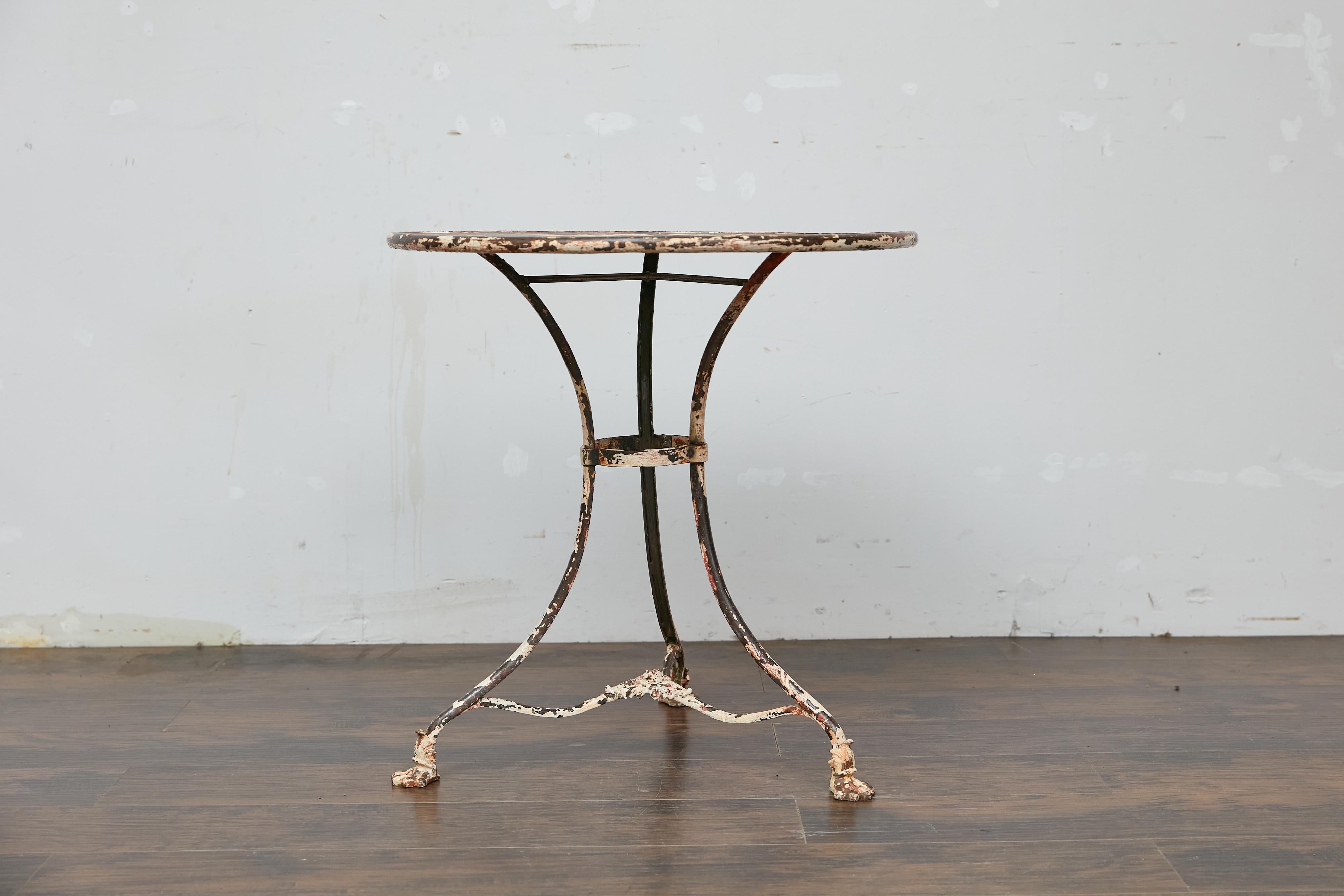 A French Turn of the Century cast iron bistro table with weathered patina. Elevate your home with this French circa 1900 cast iron bistro table, a timeless example of European craftsmanship. With its weathered painted finish and intricate claw-foot