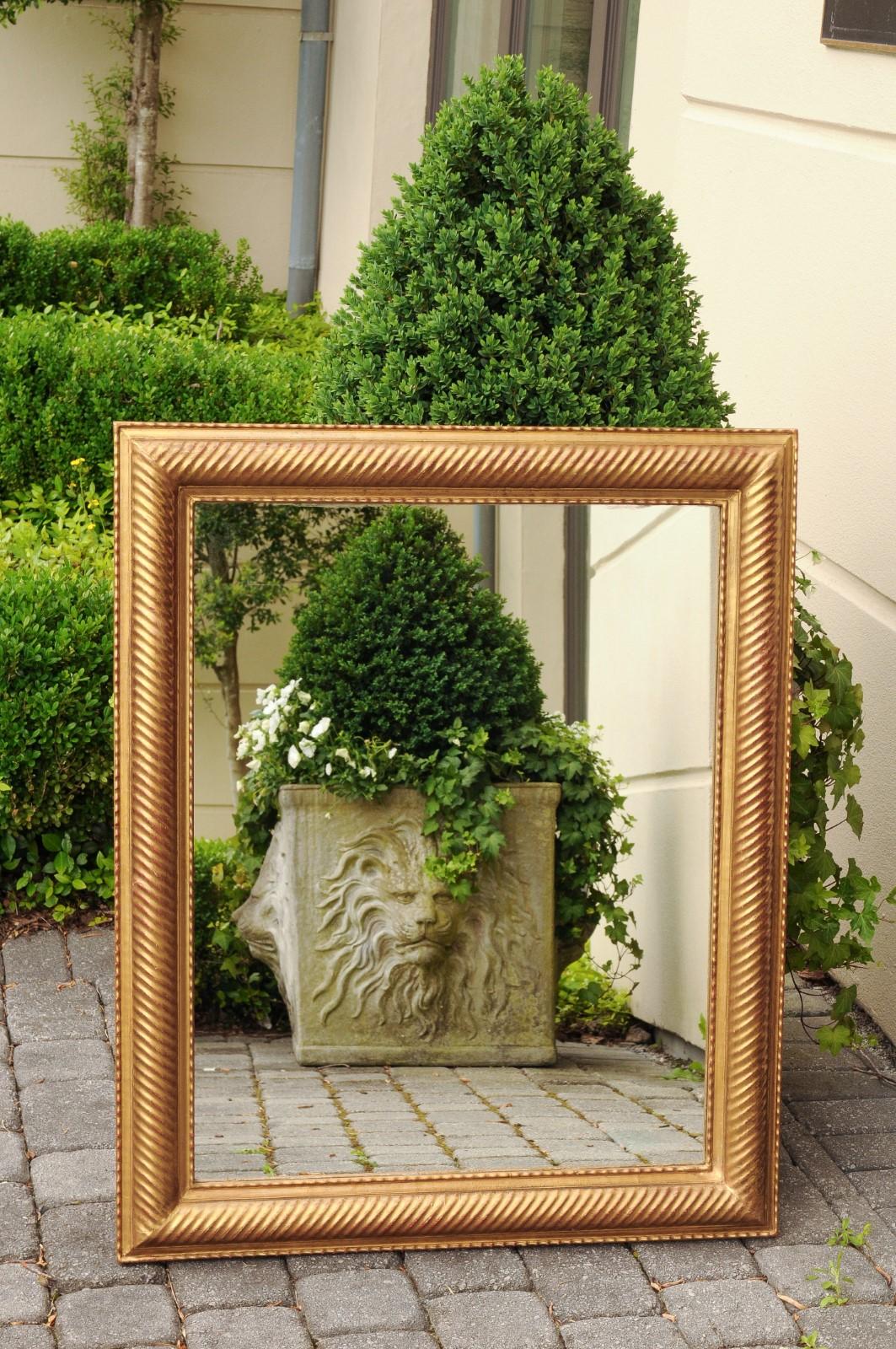 A French giltwood mirror from the early 20th century, with diagonal reeded motifs and red undertone. Born in France during the Belle-Époque era, this elegant giltwood mirror features a linear Silhouette, beautifully accented with reeded motifs