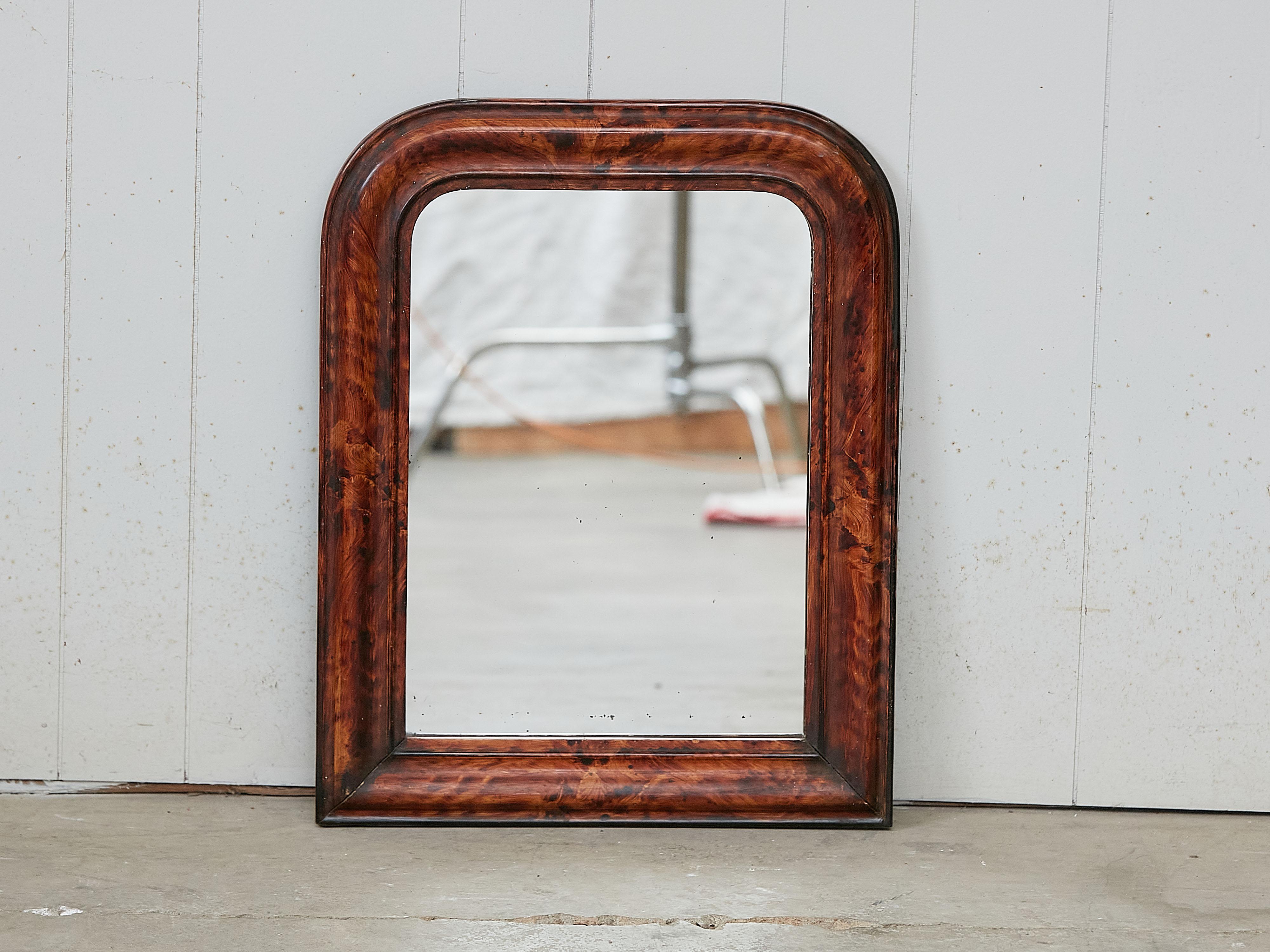 A small French Louis-Philippe style wooden mirror from the early 20th century, with faux tortoise style painted frame and rounded corners in the upper section. Created in France during the turn of the century which saw the transition between the