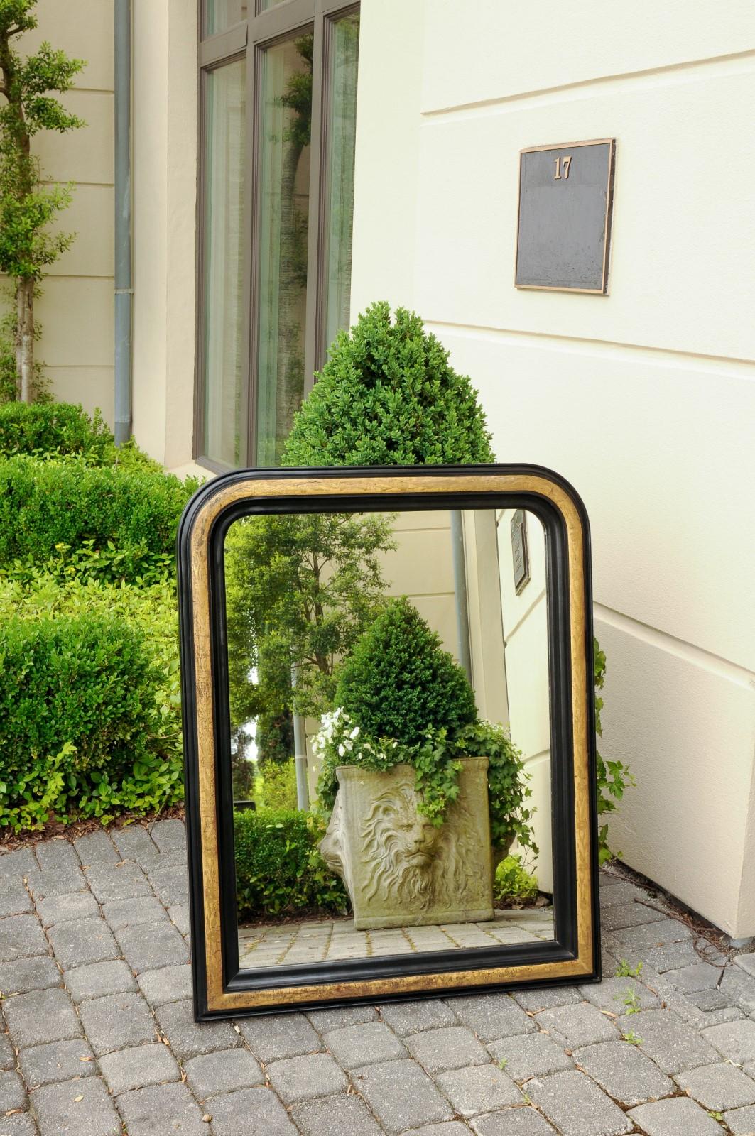 A French Louis-Philippe style wall mirror from the early 20th century, with gilded and ebonized accents. Born in France during the early years of the 20th century, this exquisite mirror presents the stylistic characteristics of the Louis-Philippe