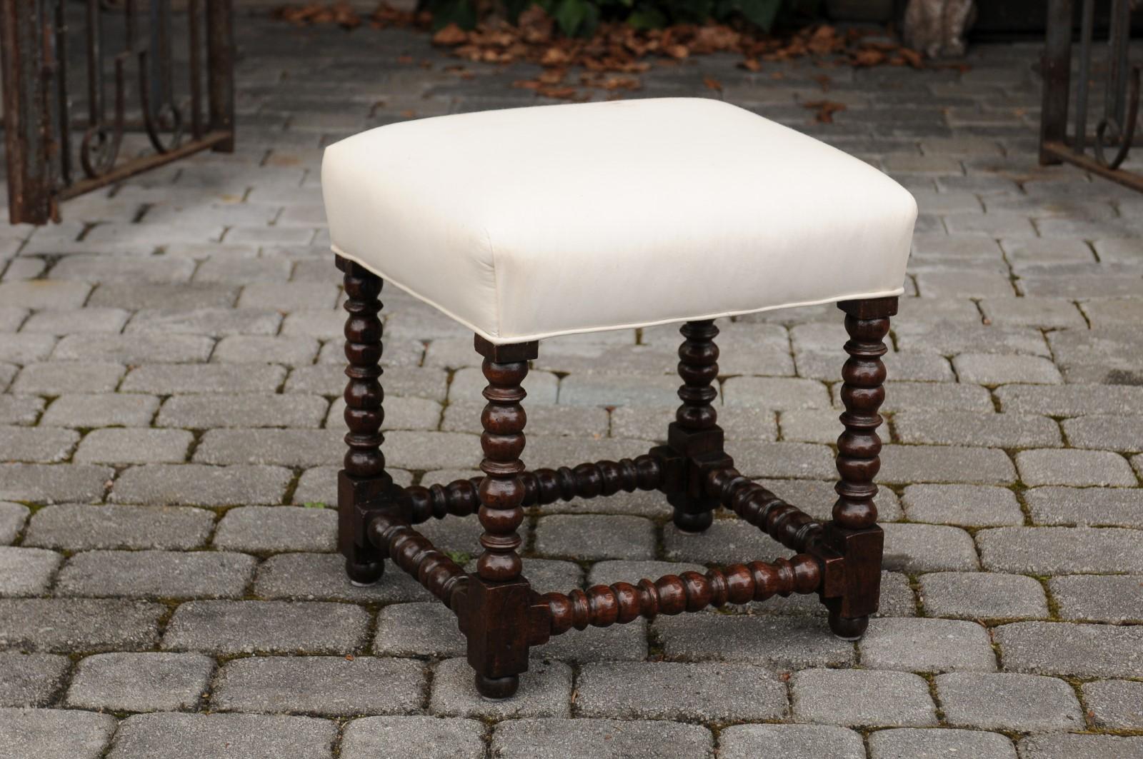 A French Louis XIII style oak stool from the early 20th century, with bobbin legs and new upholstery. Born in France at the turn of the century during the Belle Époque, this French stool features the stylistic characteristics of the Louis XIII era.