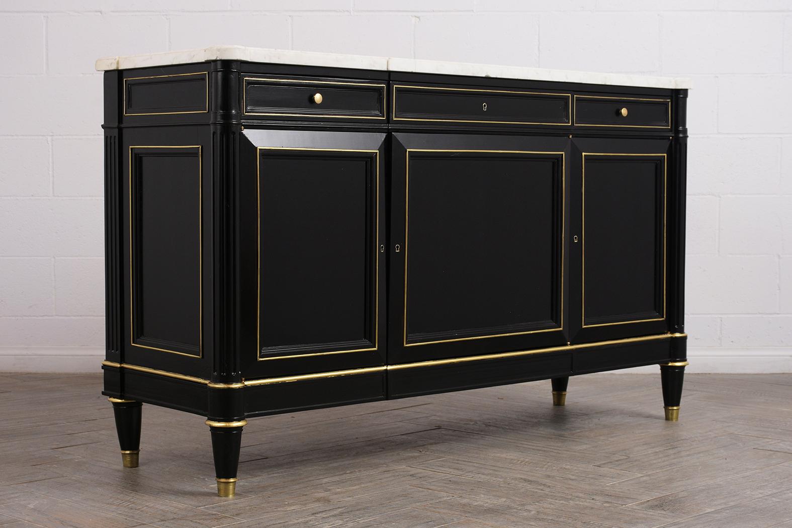 This 1900s Louis XVI-style mahogany buffet has the original white Carrara marble top with beveled edges, elegant ebonized and polished finish. The buffet has three drawers along the top, and centre drawer has a brass keyhole and lock. The bottom has