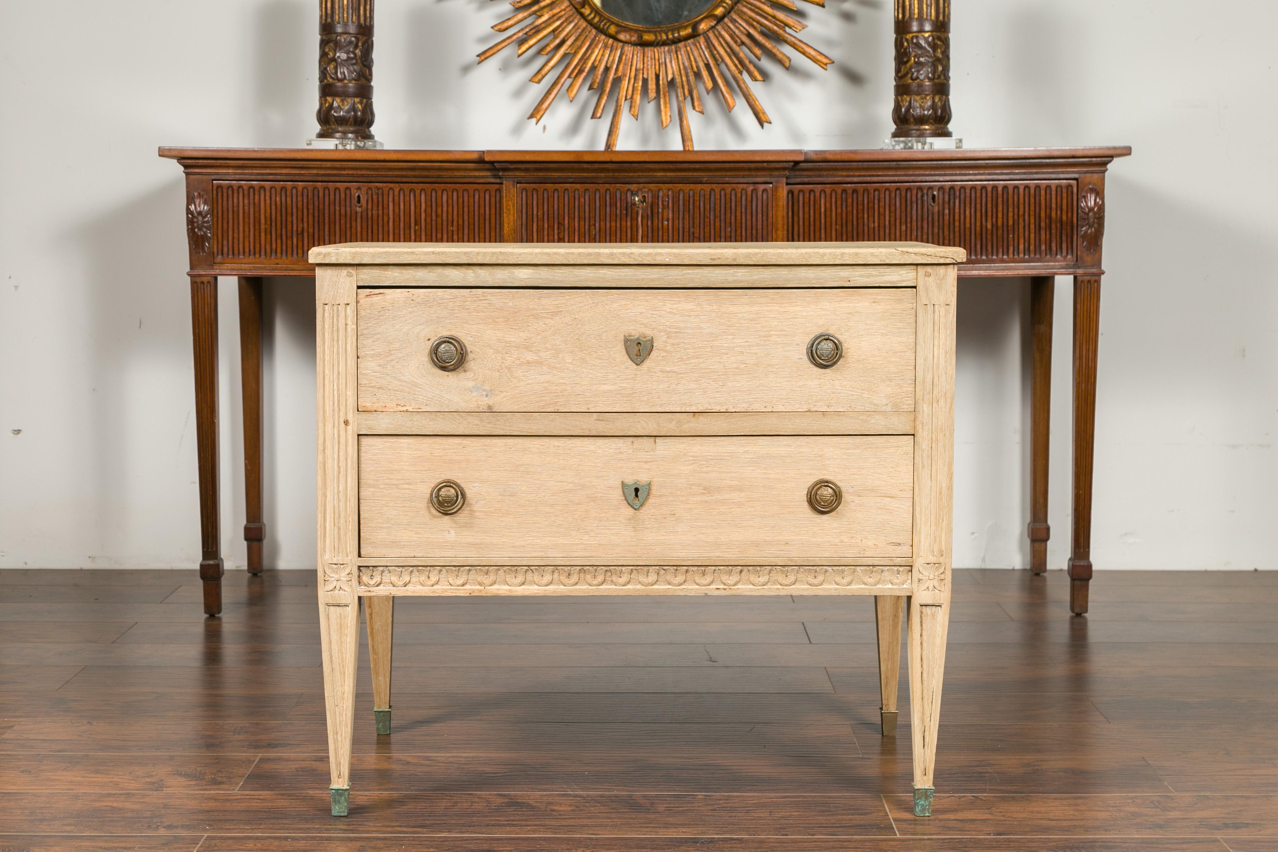 A French neoclassical style bleached wood commode from the early 20th century, with carved campanula motifs and tapered legs. Crafted in France during the early years of the 20th century, this neoclassical style commode features a rectangular top