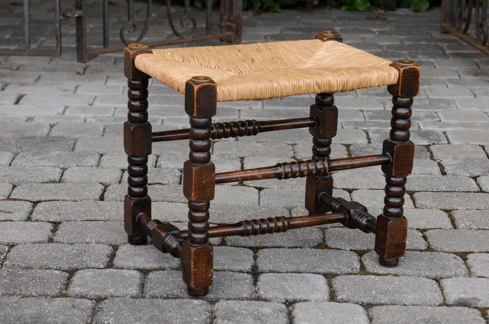 A French oak stool from the early 20th century, with turned legs and rush seat. Born in France during the turn of the century, this charming oak stool features a rectangular rush seat resting on a turned base made of four legs with bobbin accents,