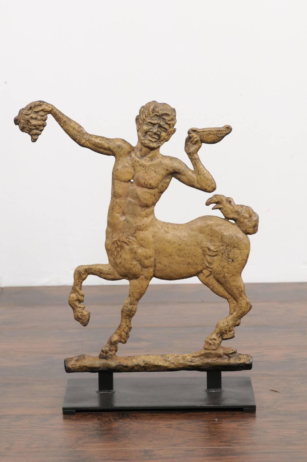 A French painted iron centaur sculpture from the early 20th century, mounted on a custom base. This French decorative object features a theme borrowed from the Greco-Roman mythology, a centaur, half-man half-horse, holding with pride grapes in his